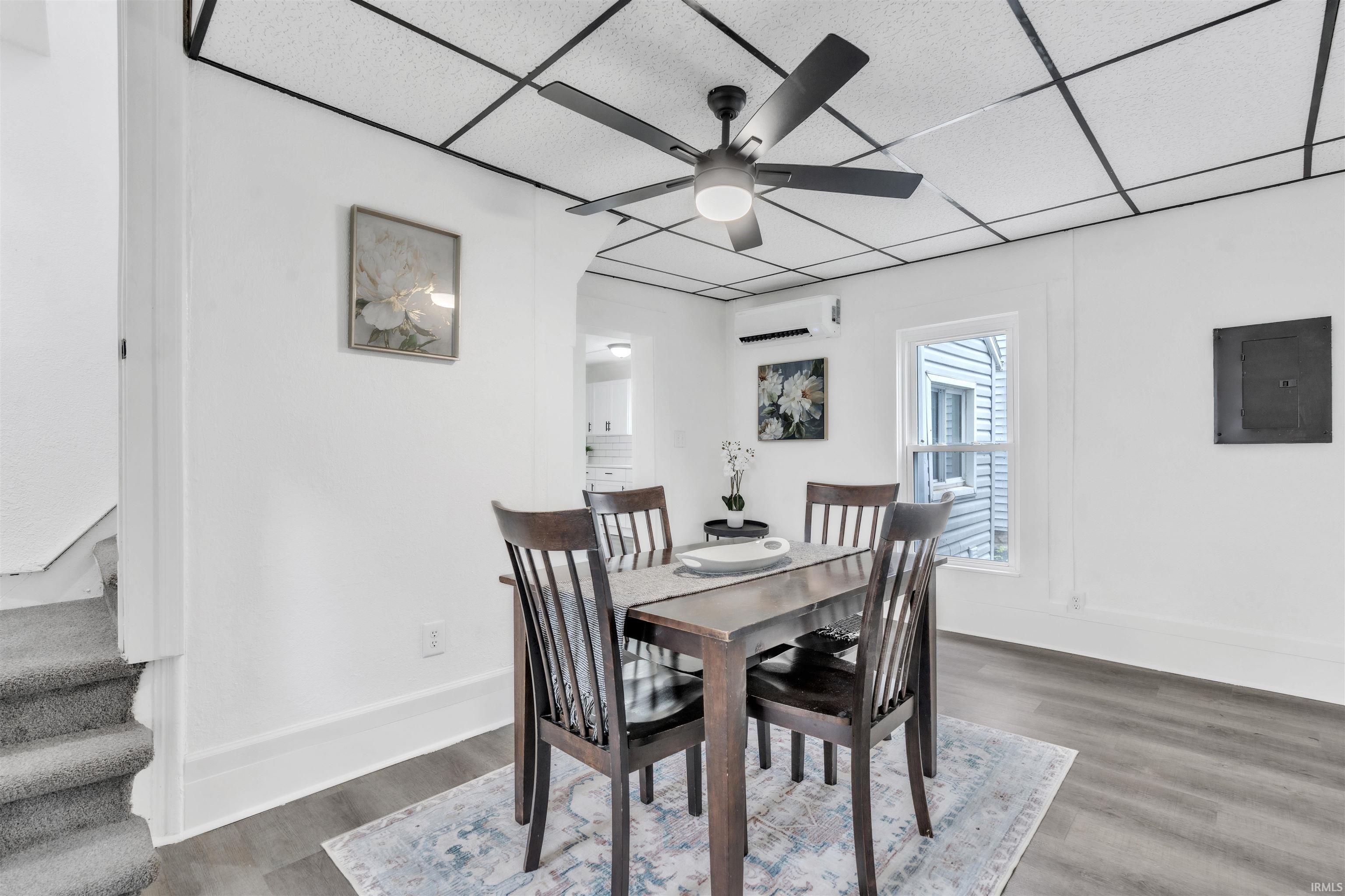 Dining area featuring wood-finish flooring, a ceiling fan with integrated lighting, white walls, a single-pane window, and an installed wall-mounted air conditioning unit
