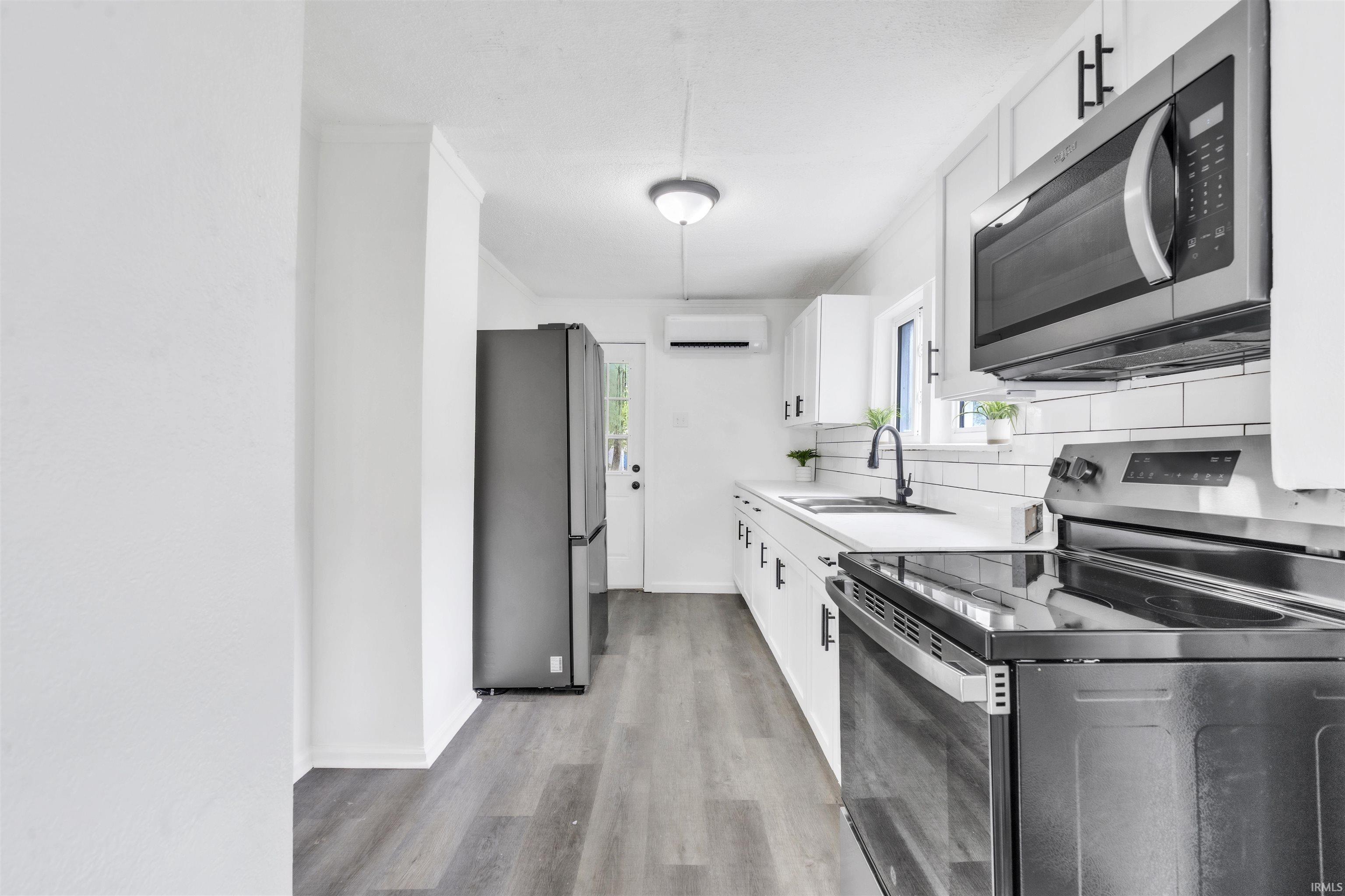 Modern kitchen featuring white cabinetry, gray wood-finish flooring, white subway tile backsplash, stainless steel appliances, and a matte black faucet