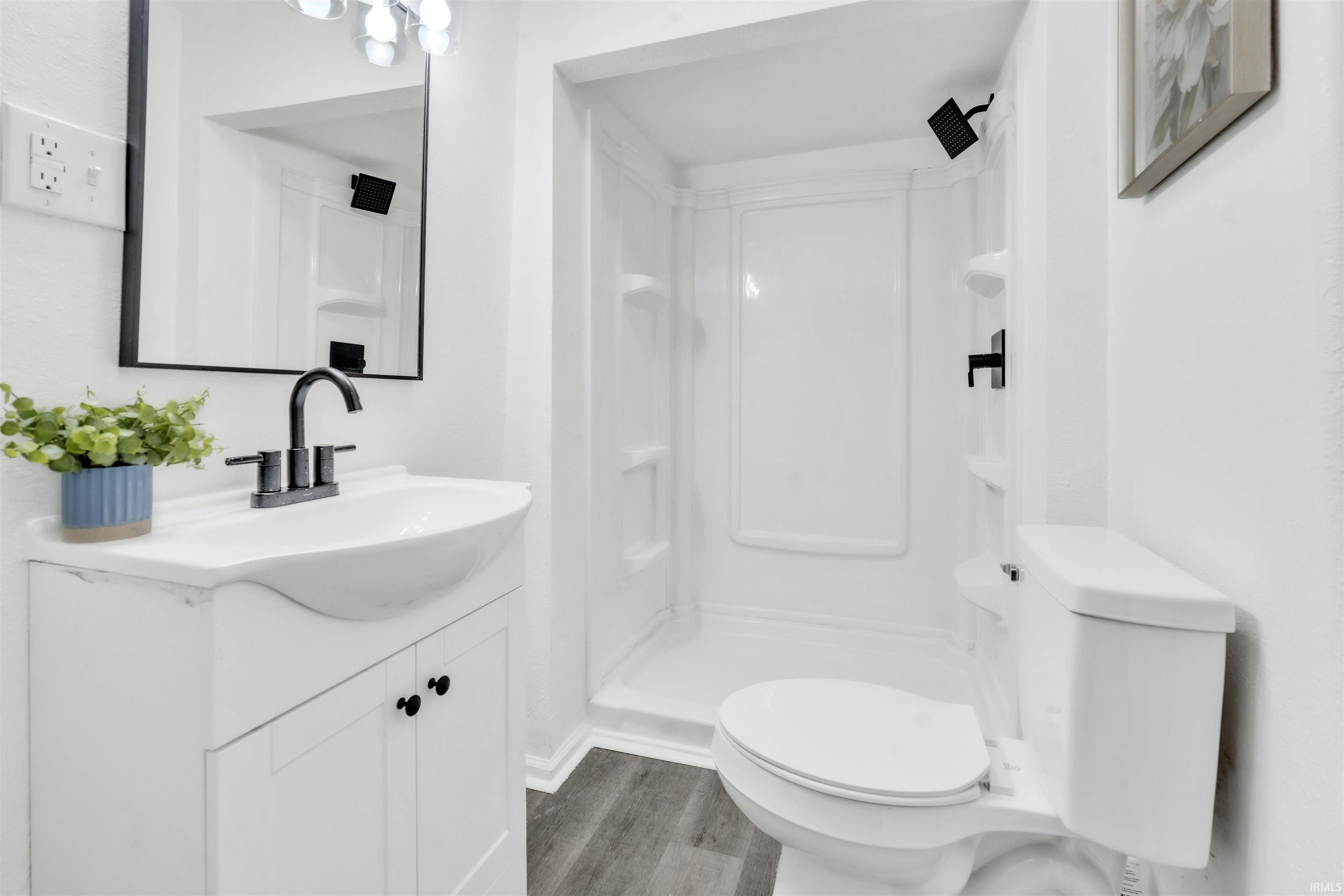 Bathroom featuring a white vanity with integrated sink, matte black faucet, wall-mounted mirror with black frame, and a stand-up shower with a single-handle fixture