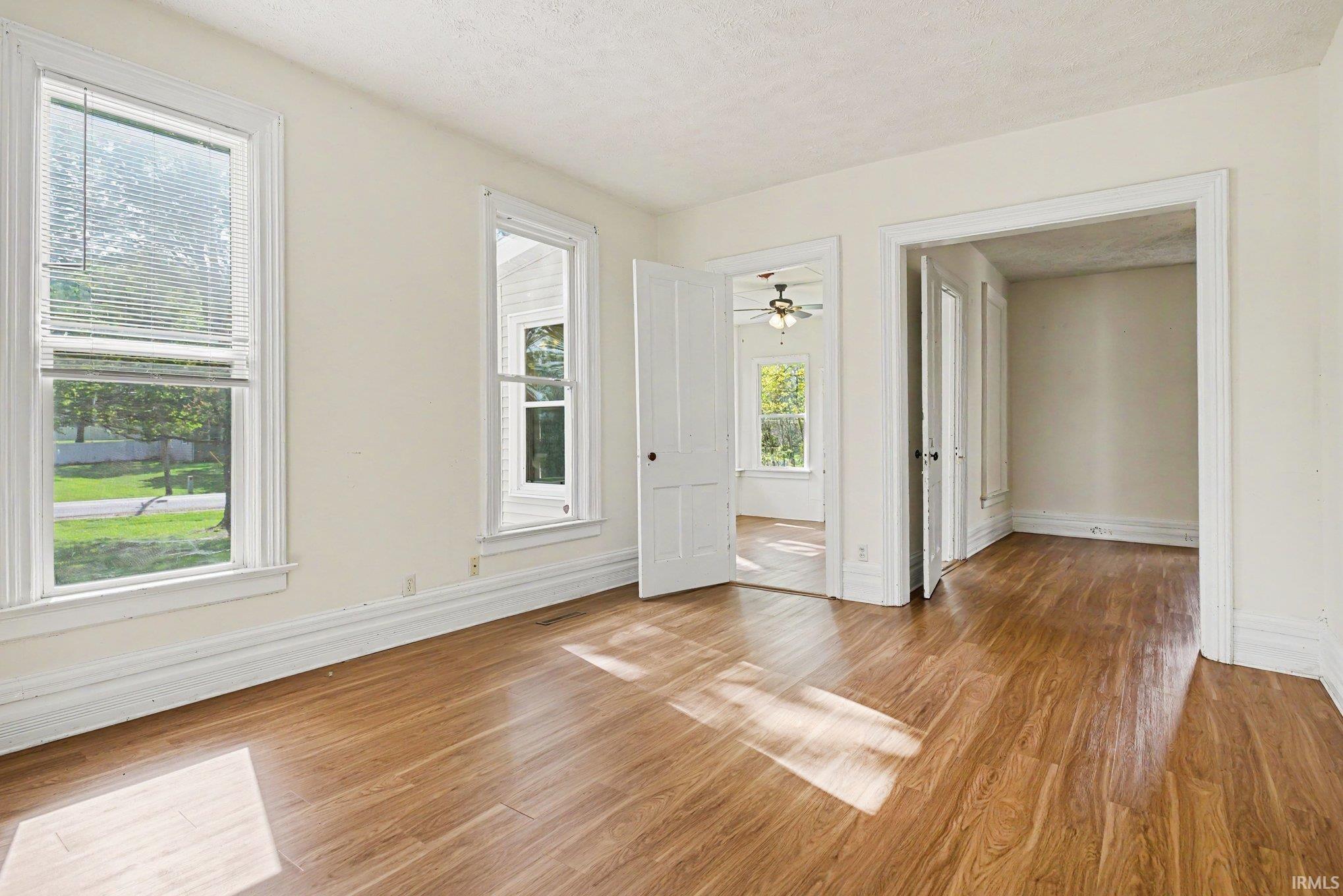 Room featuring wood-finish flooring, white trim, multiple windows with blinds, and two doorways leading to additional spaces
