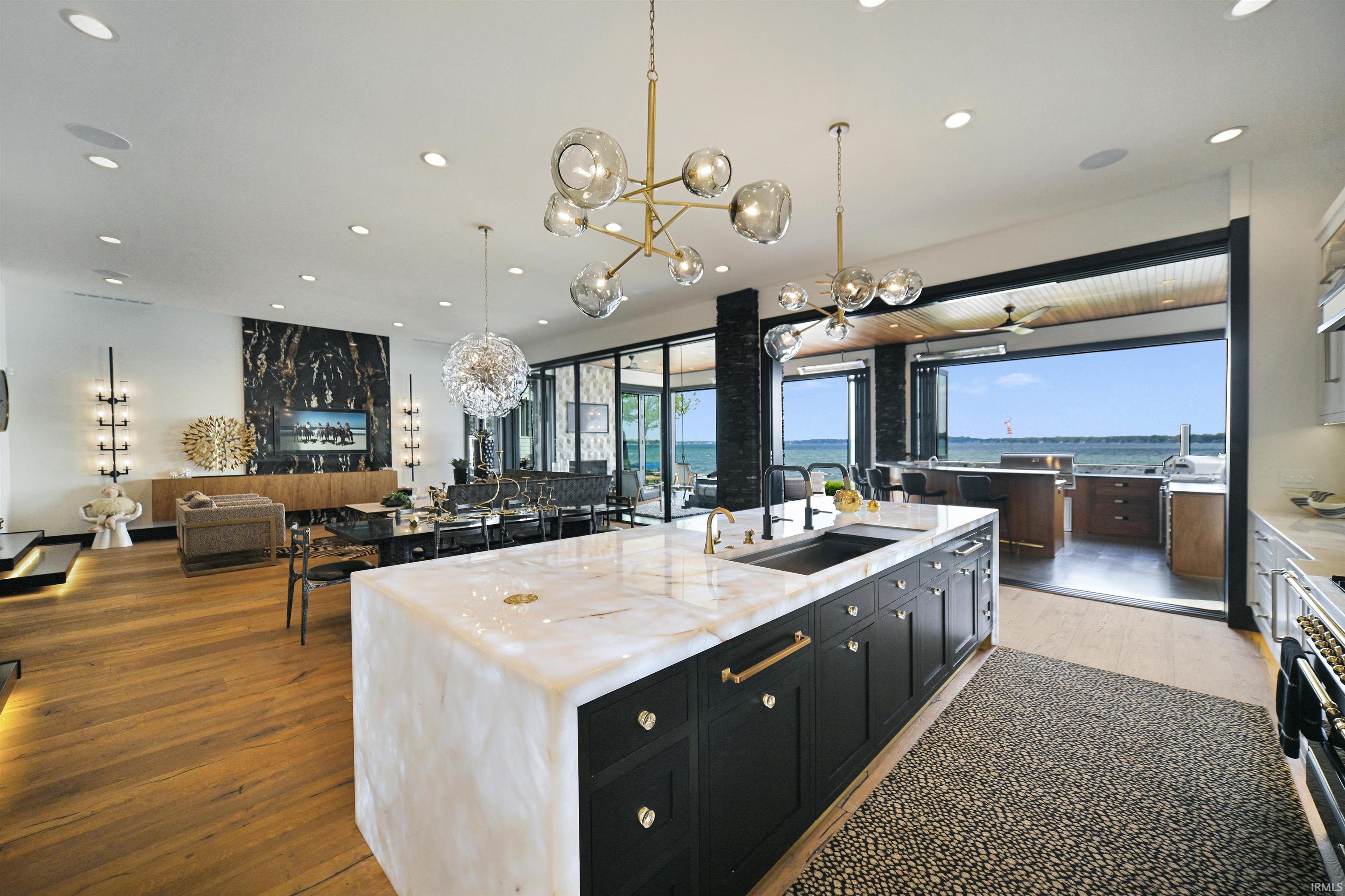 Gourmet kitchen featuring an oversized waterfall island with an integrated sink, custom dark cabinetry, and high-end built-in appliances