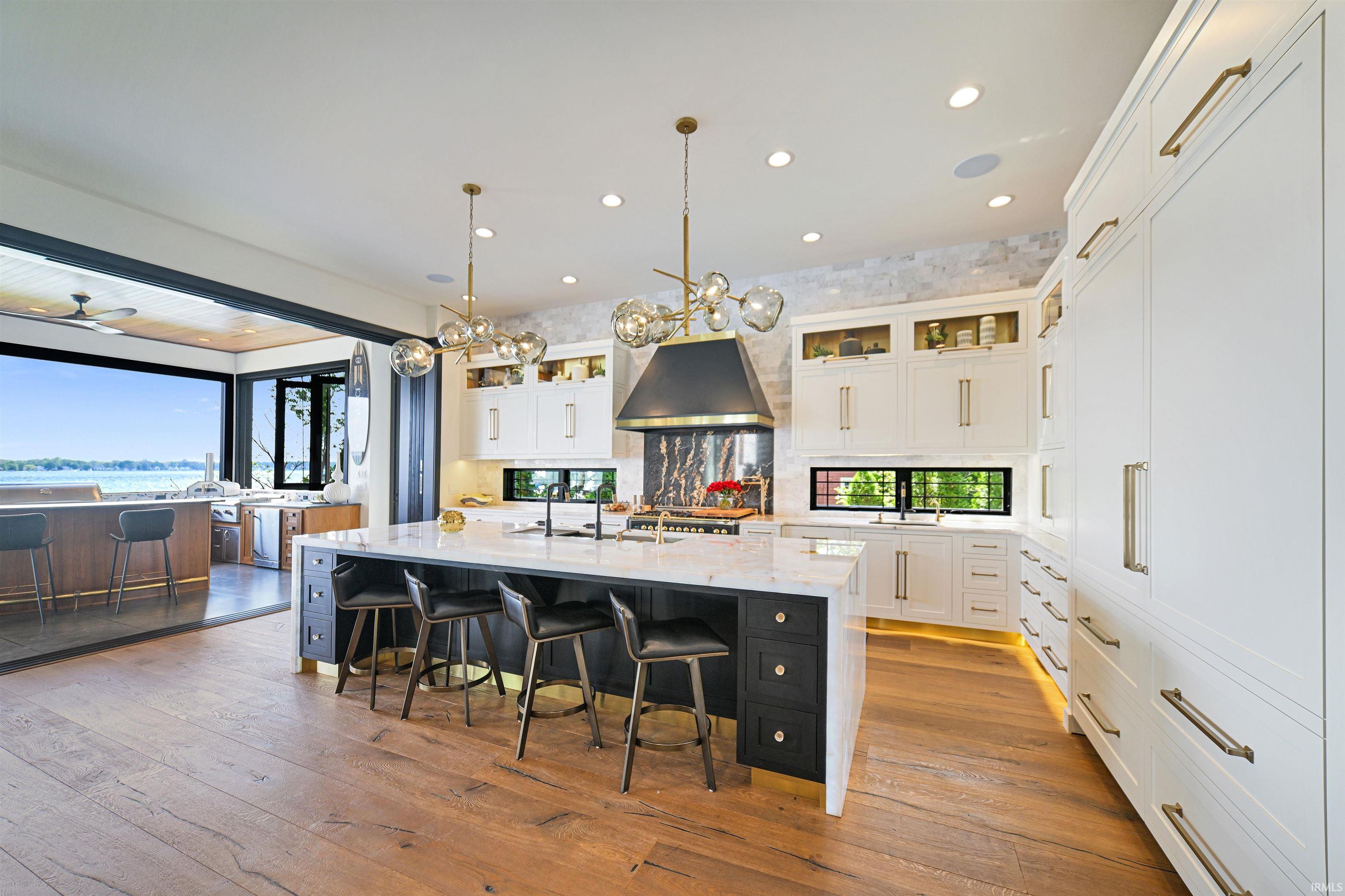 Gourmet kitchen featuring a large central island with seating, white perimeter cabinetry, wood-finish flooring, a contemporary range hood, and modern pendant lighting