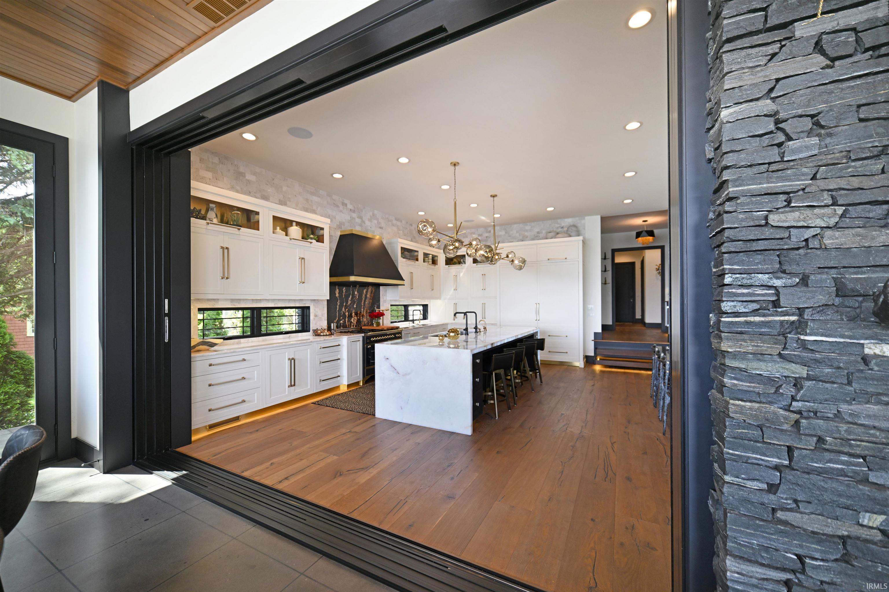 Gourmet kitchen featuring a waterfall island with seating, white cabinetry, integrated appliances, and wood-finish flooring