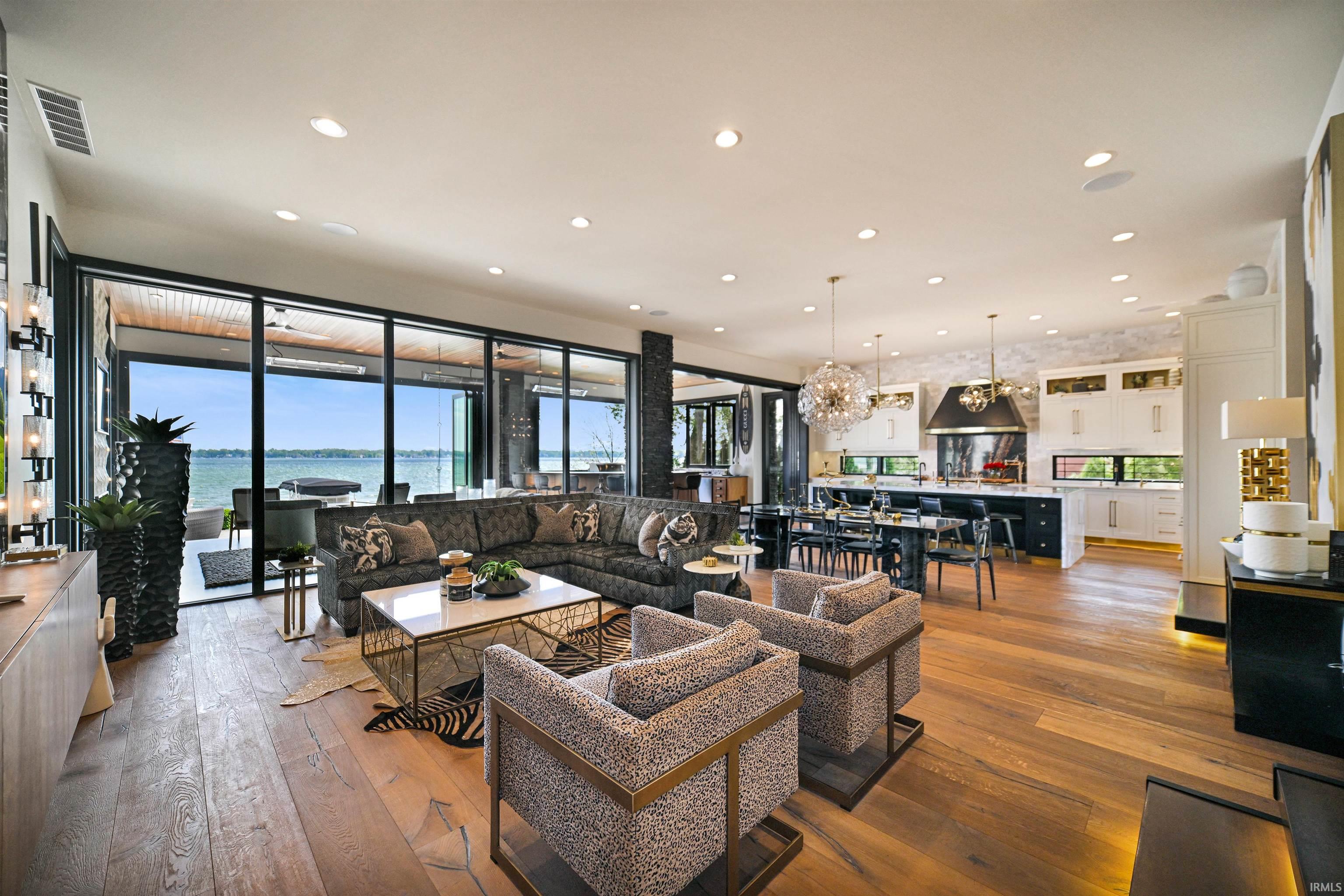 Expansive open-concept interior featuring wood-finish flooring, a contemporary kitchen with white and black cabinetry, and a dining area with modern pendant lighting