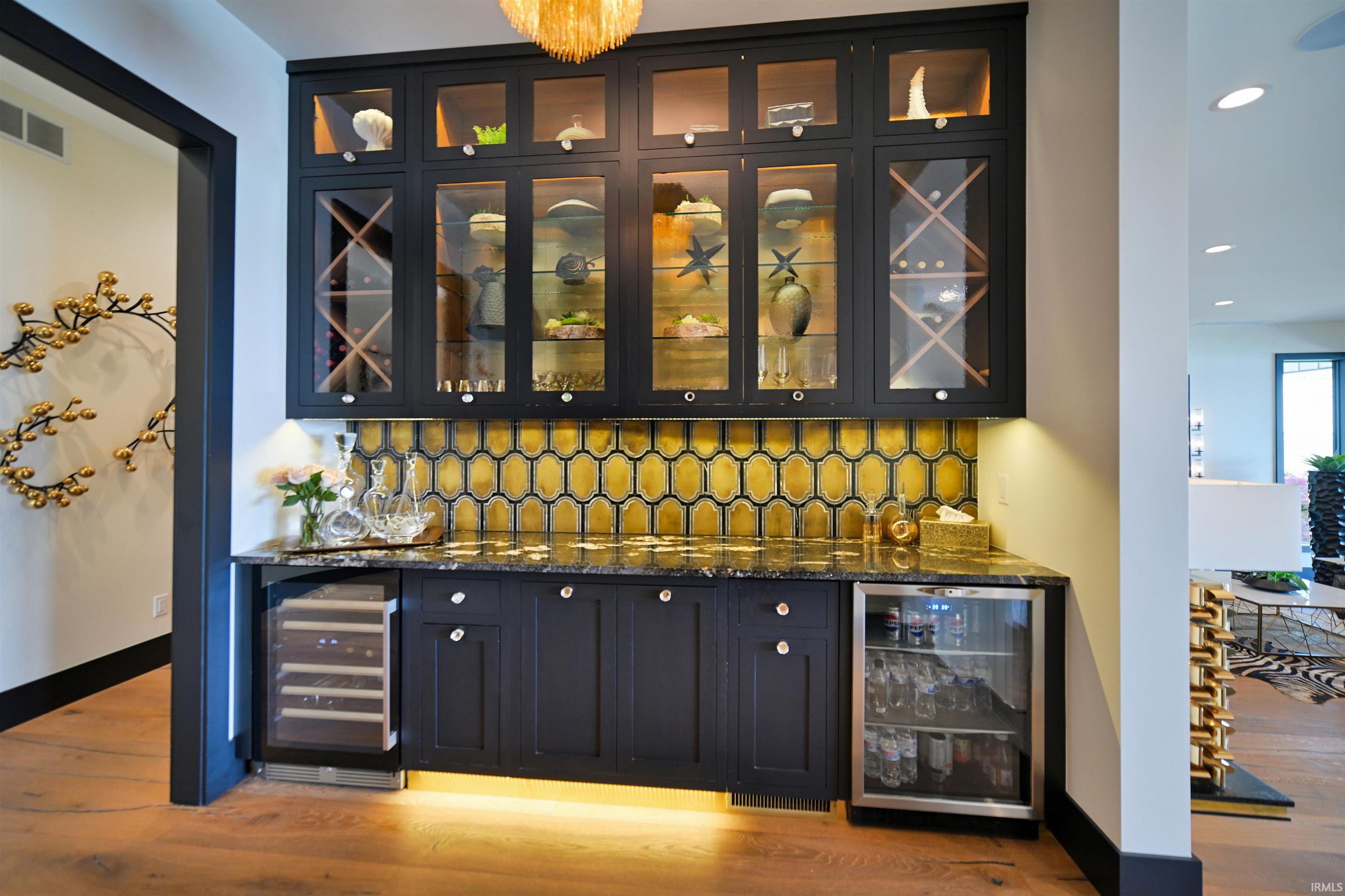 Built-in bar with dark cabinetry, integrated beverage refrigerators, and a golden hexagonal tile backsplash