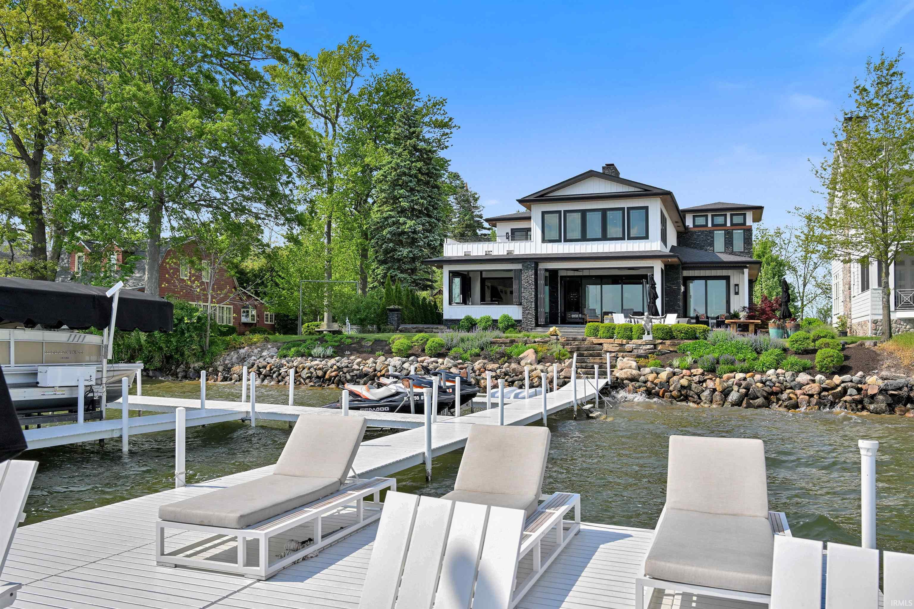 Waterfront property featuring a private dock system, a contemporary house with dark-framed windows, a stone and white siding exterior, and a terraced landscape with natural rock hardscaping