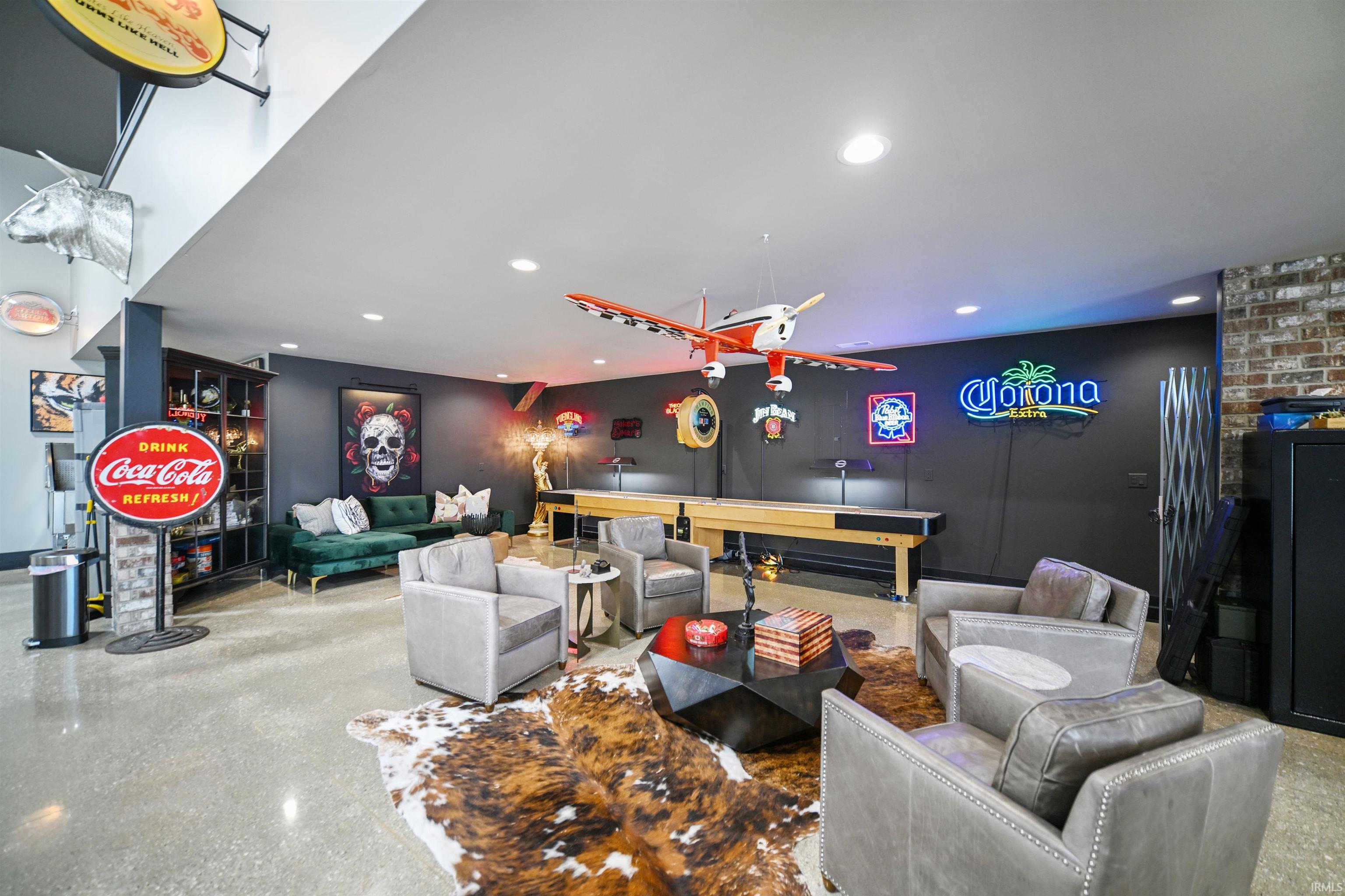 Spacious recreation area featuring polished concrete flooring, recessed lighting, exposed brick accents, and a built-in shuffleboard table