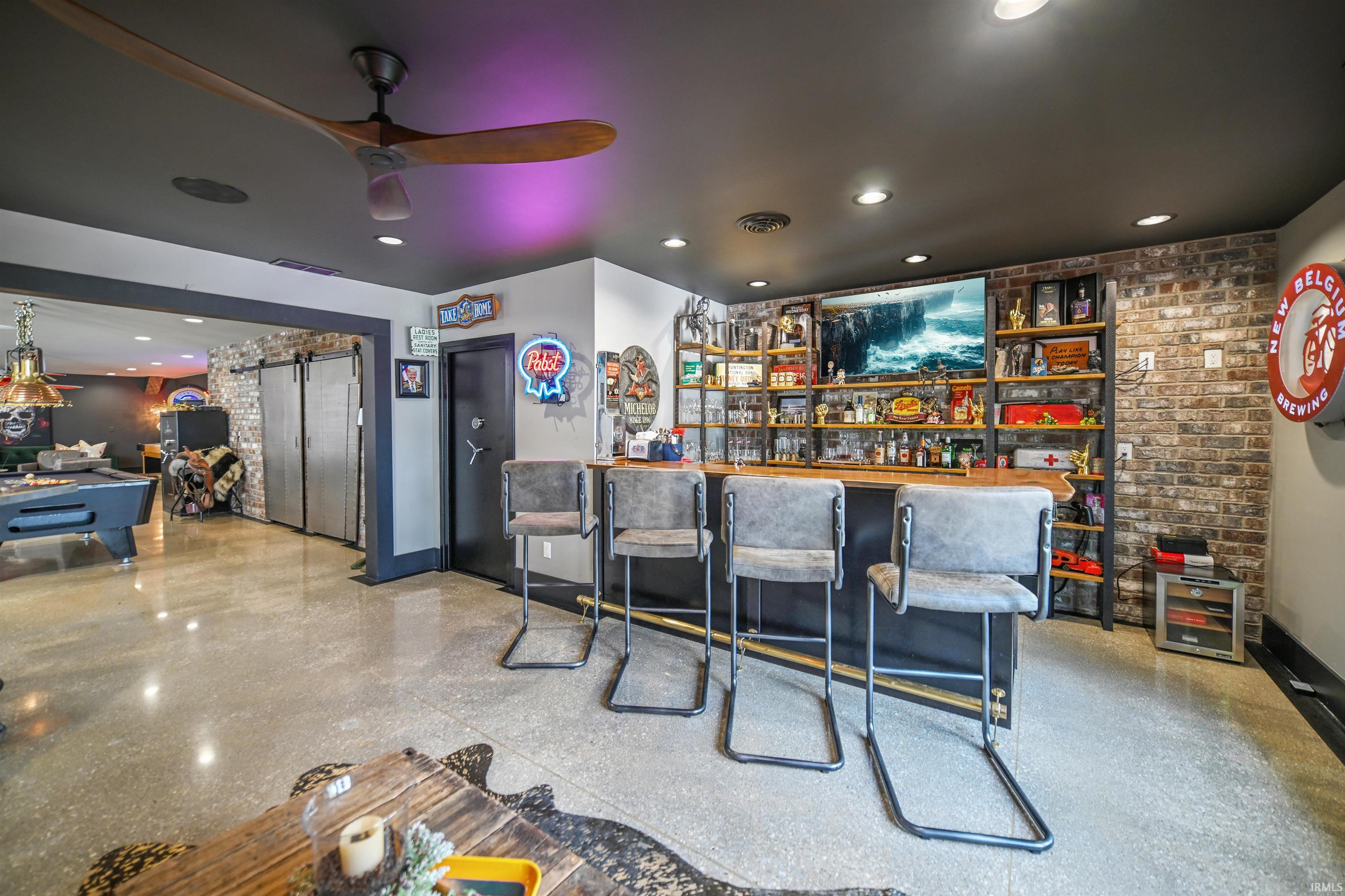 Custom bar area featuring exposed brick accent wall, wood-finish shelving, recessed lighting, and polished concrete flooring