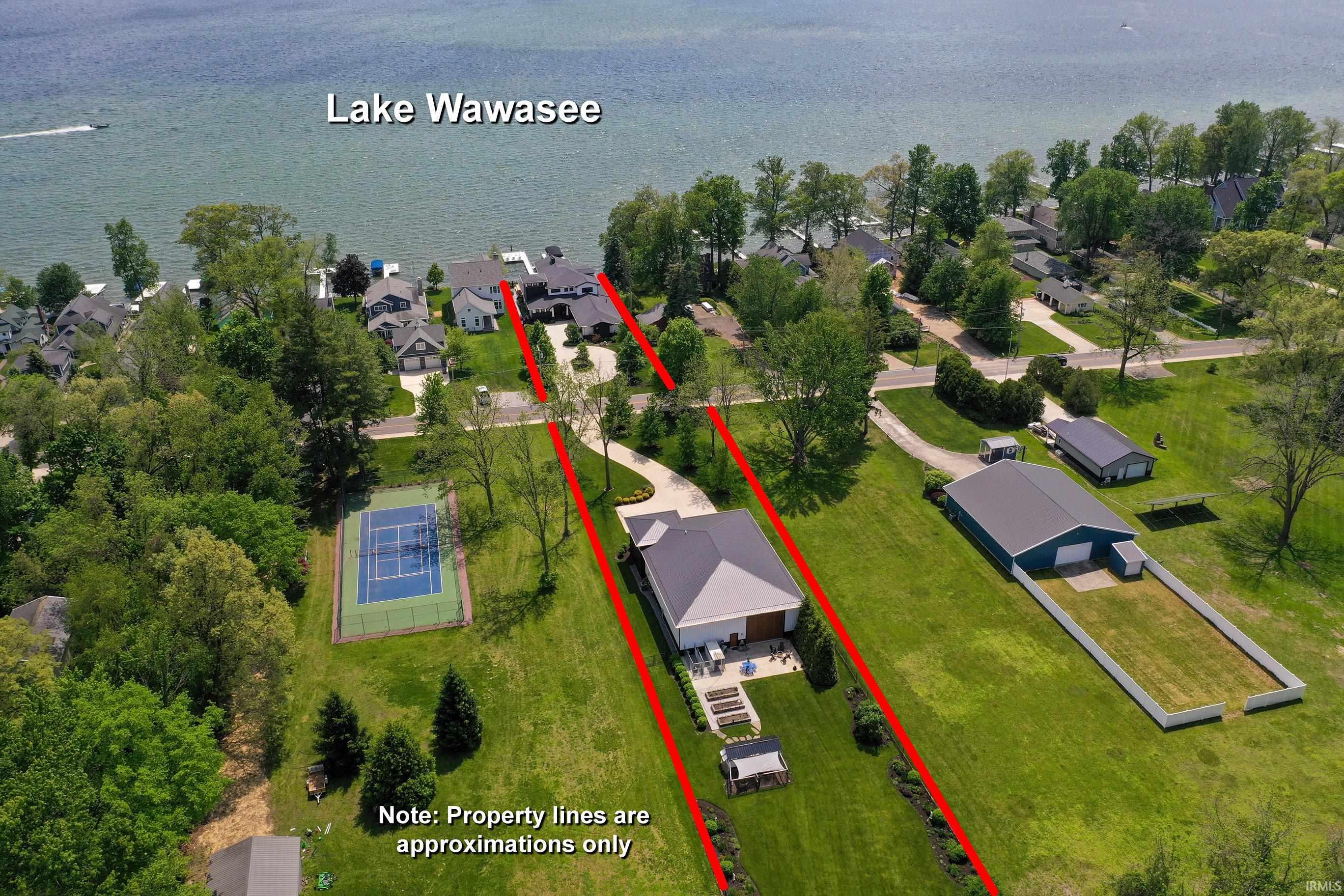 Lake Wawasee waterfront property featuring an extensive green lawn, private tennis court, and a large additional structure