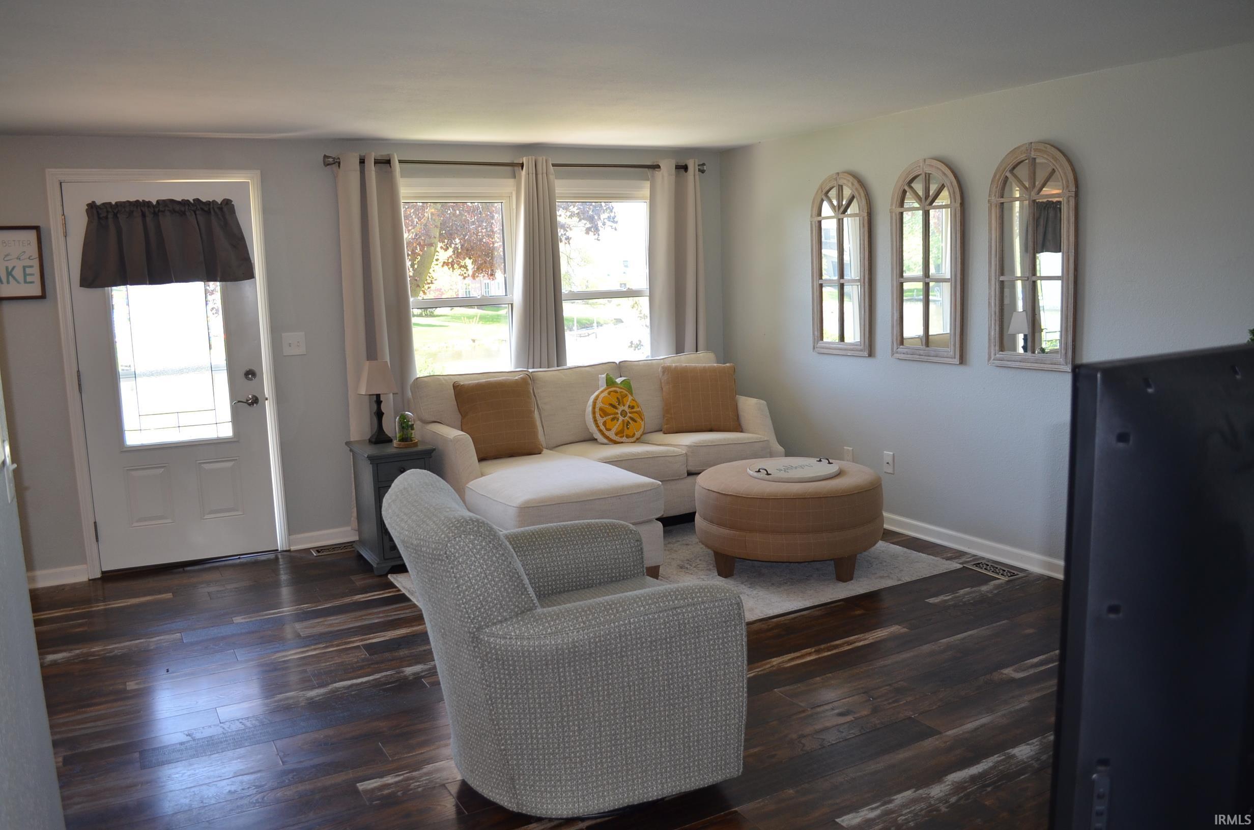 Spacious living area featuring dark wood-finish flooring, light gray walls, and large windows with natural light