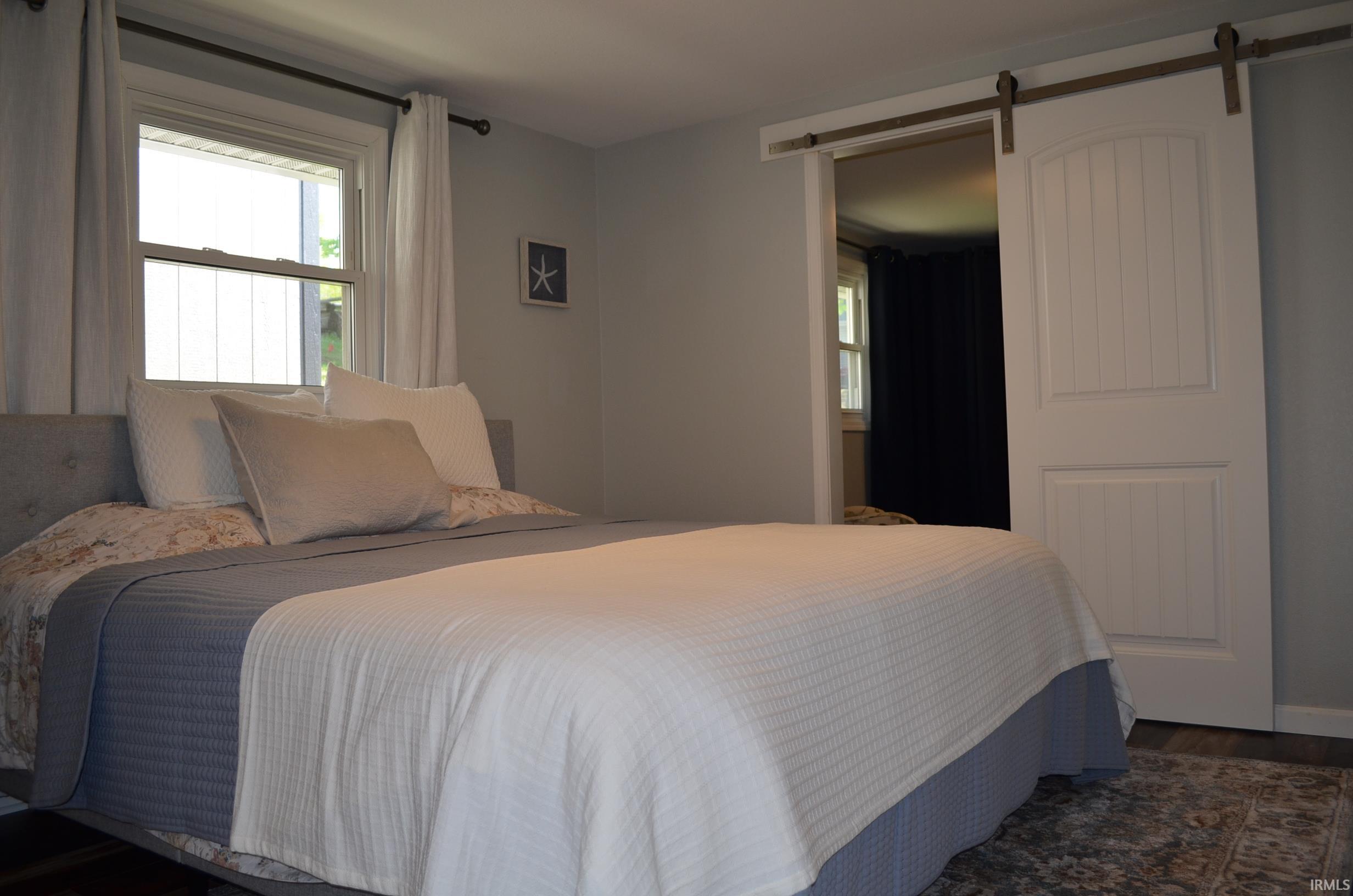 Interior room featuring a barn door entry, wood-finish flooring, and a single window with white drapery