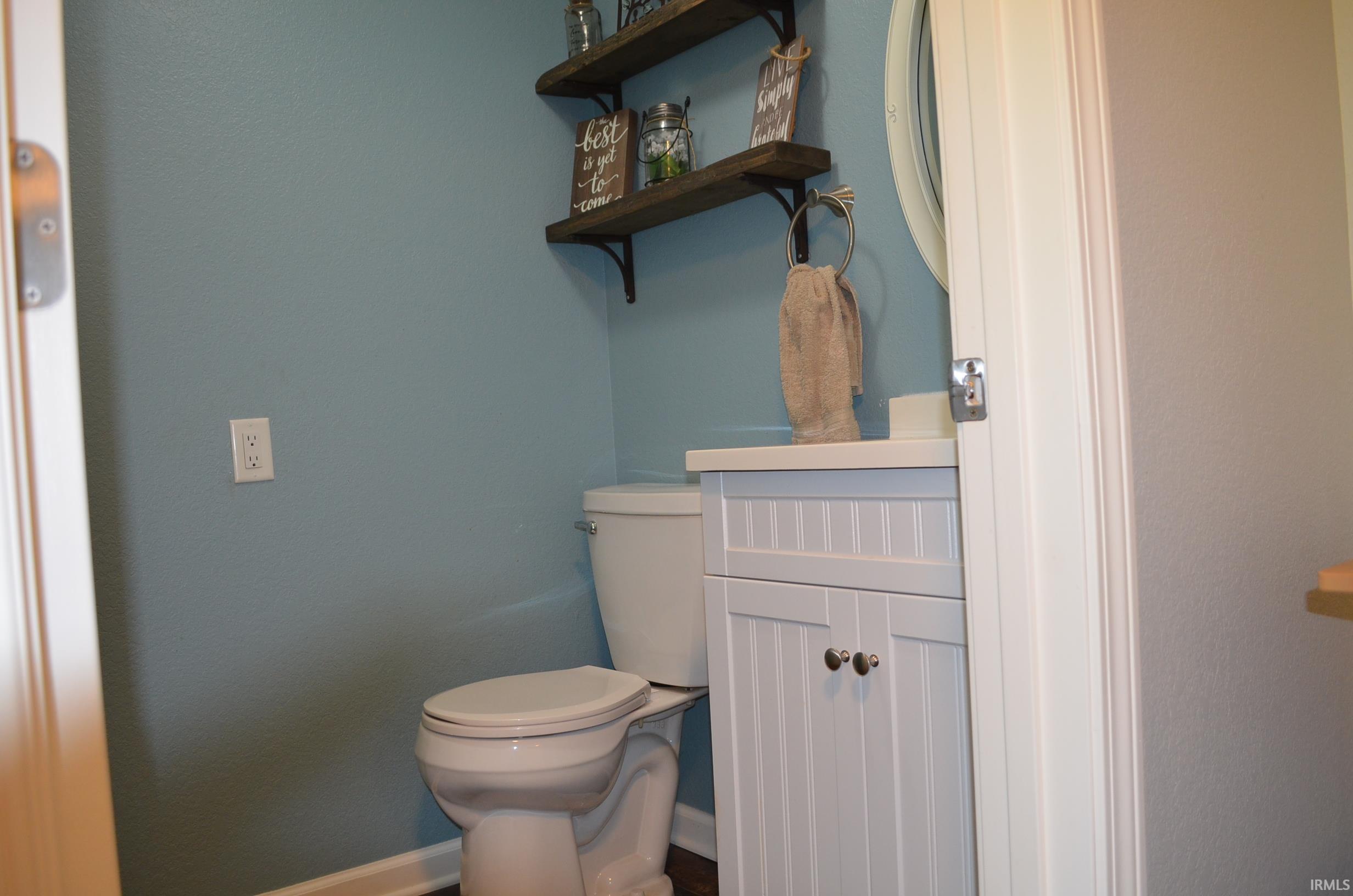 Powder room featuring a white beadboard vanity with cabinet storage, a white countertop, and a circular mirror