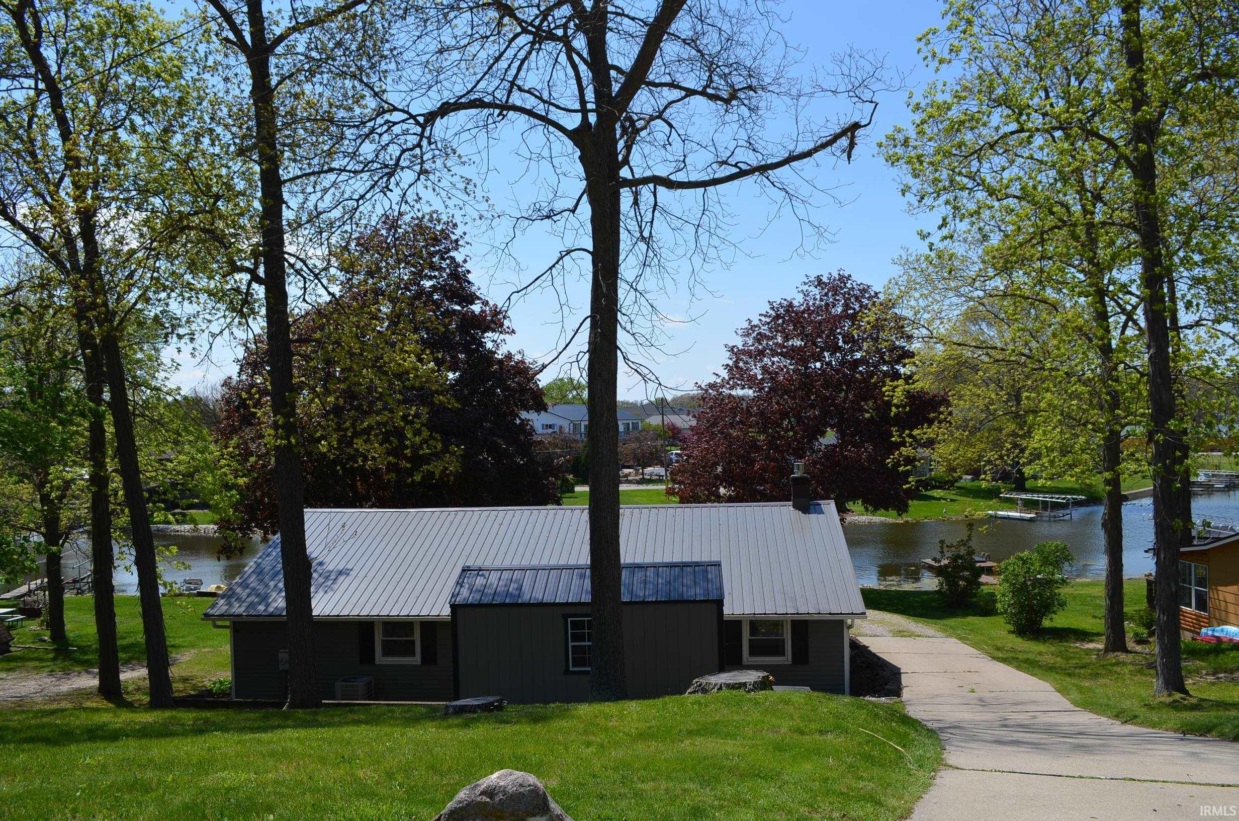 Waterfront property featuring a charcoal blue siding exterior, a silver metal roof, and a paved driveway