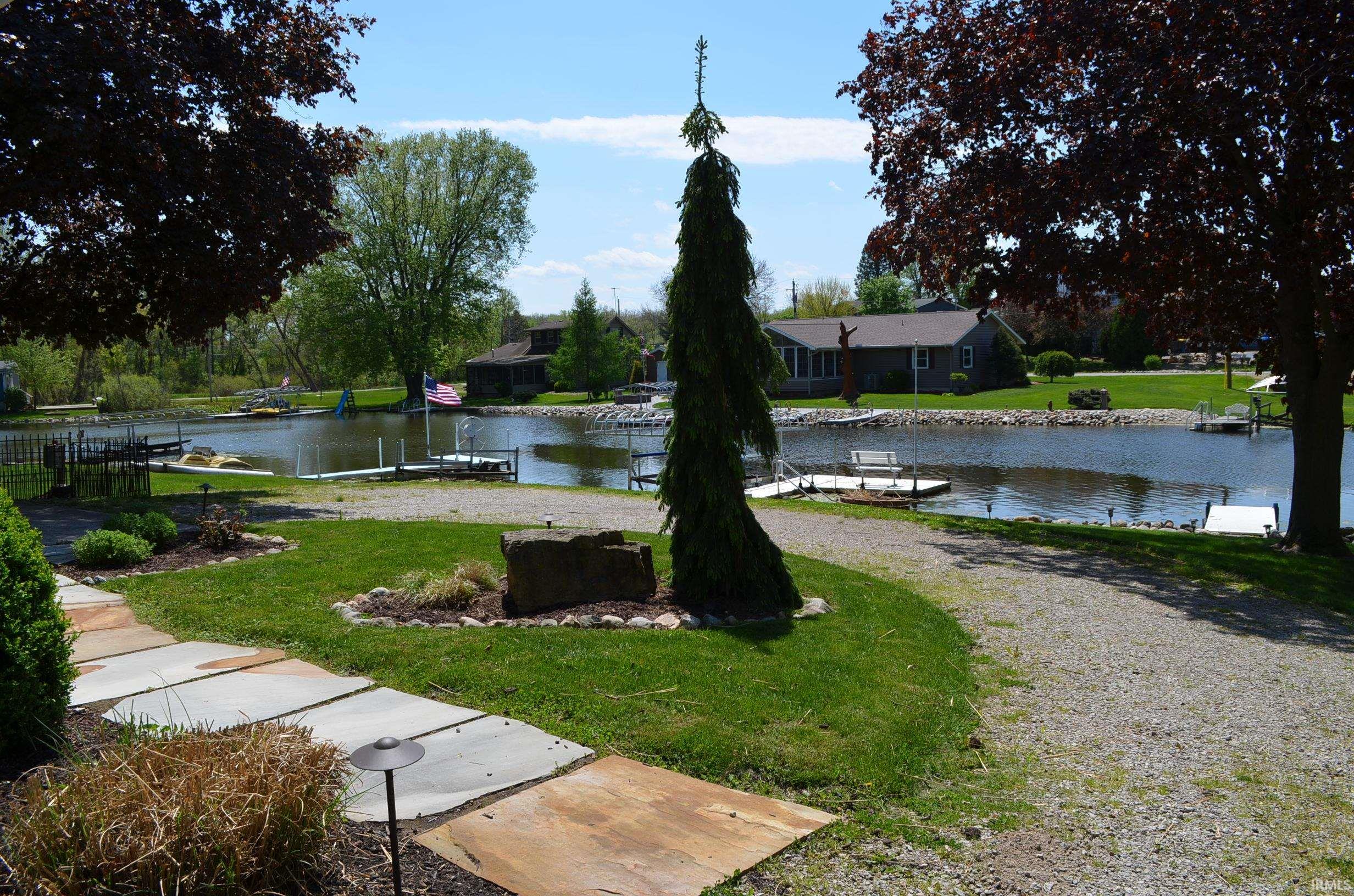 Waterfront setting with multiple private docks, a stone paver pathway, gravel driveway, and mature landscaping