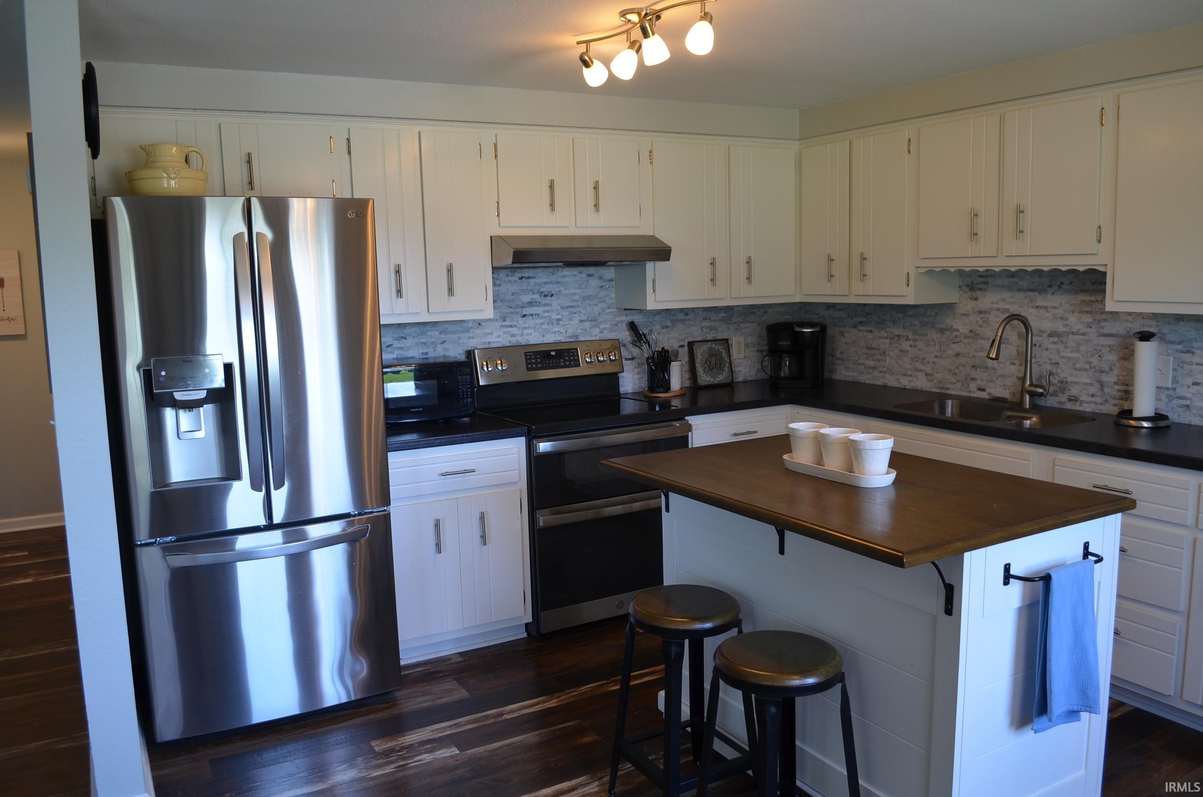 Kitchen featuring white cabinetry, dark countertops, a mosaic tile backsplash, stainless steel appliances, and wood-finish flooring