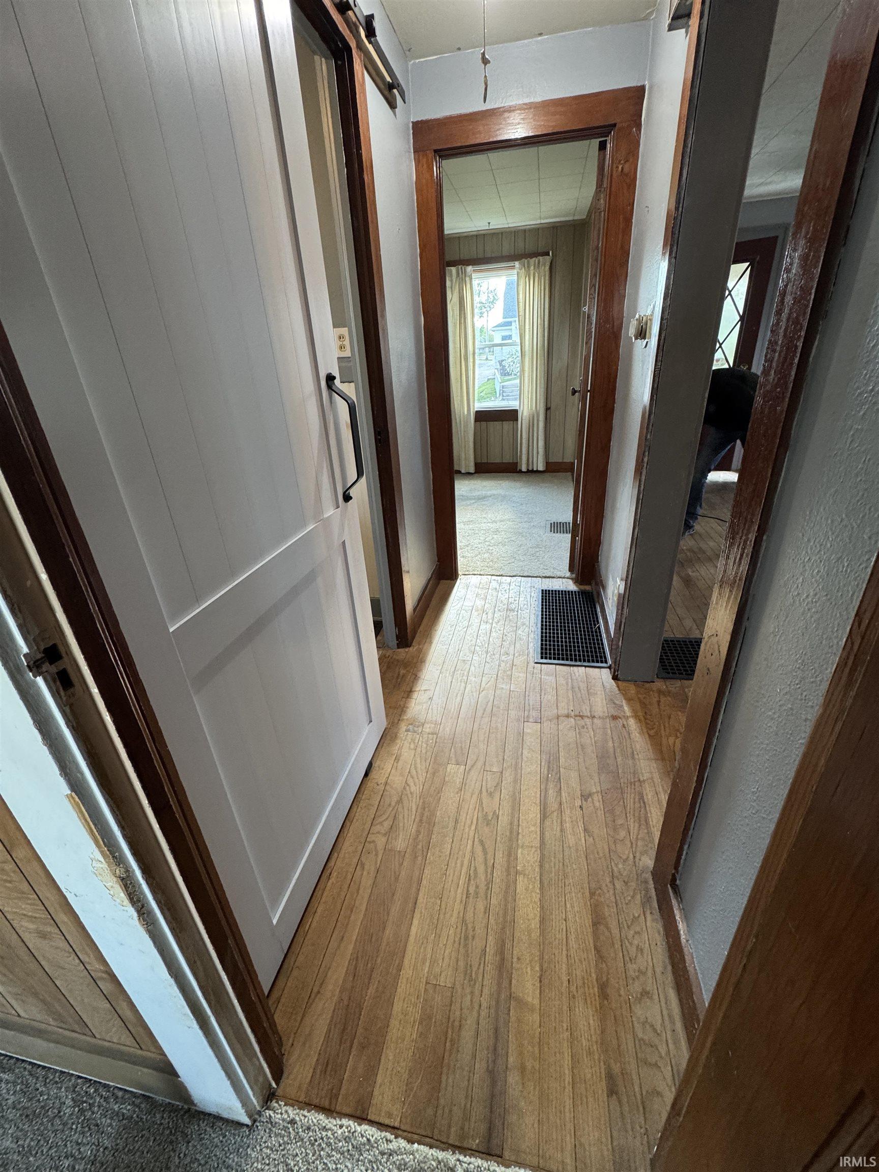 Hallway featuring wood-finish flooring, a white sliding barn door, and dark wood trim