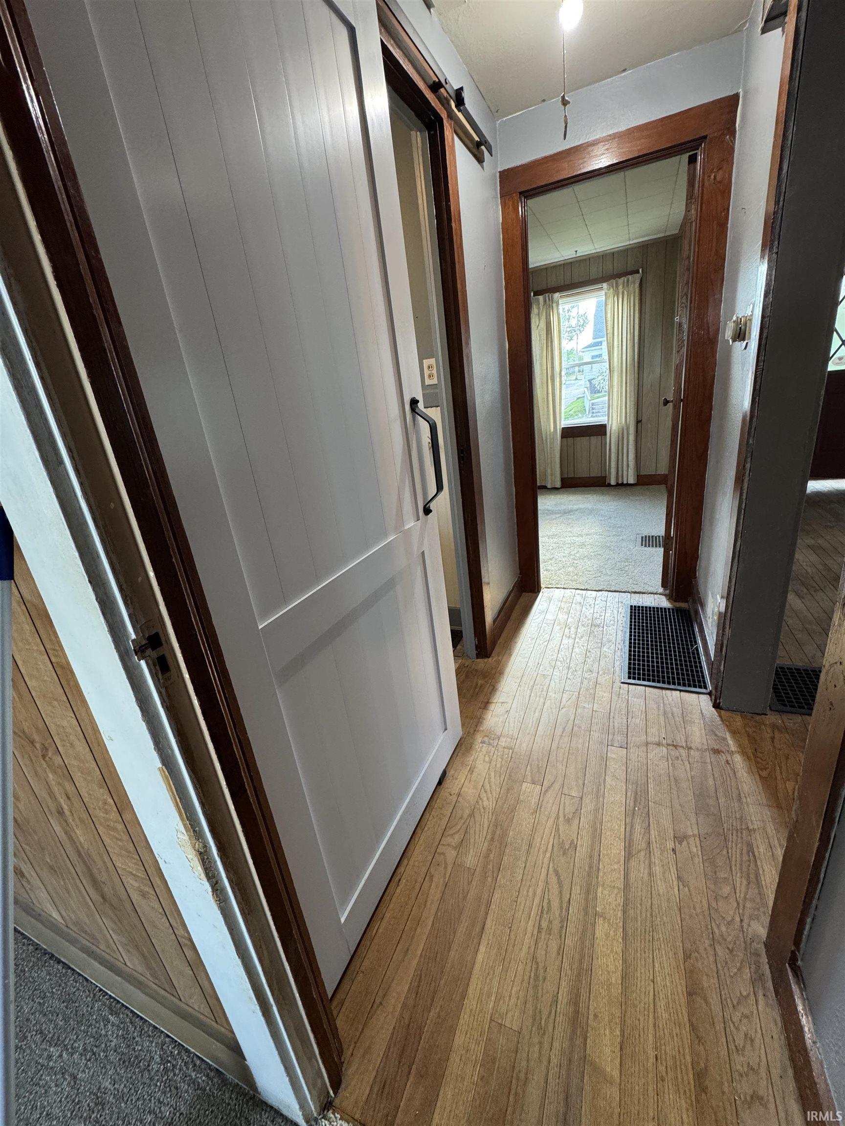 Wood-finish flooring extending through a hallway, featuring a modern white barn door with black hardware