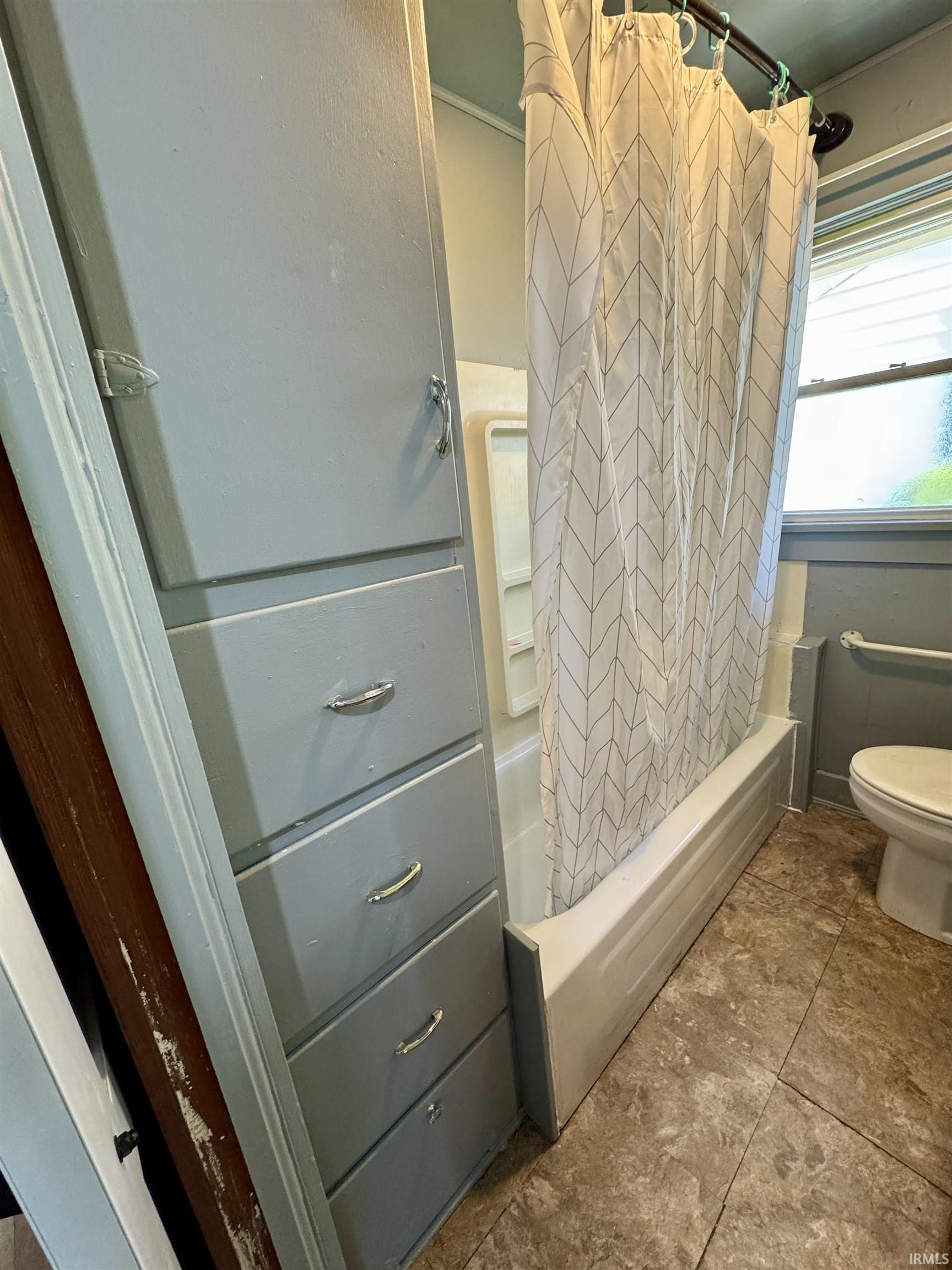 Bathroom featuring built-in cabinetry with four drawers and an upper cabinet, a bathtub with a white shower curtain, a window, and a tile floor