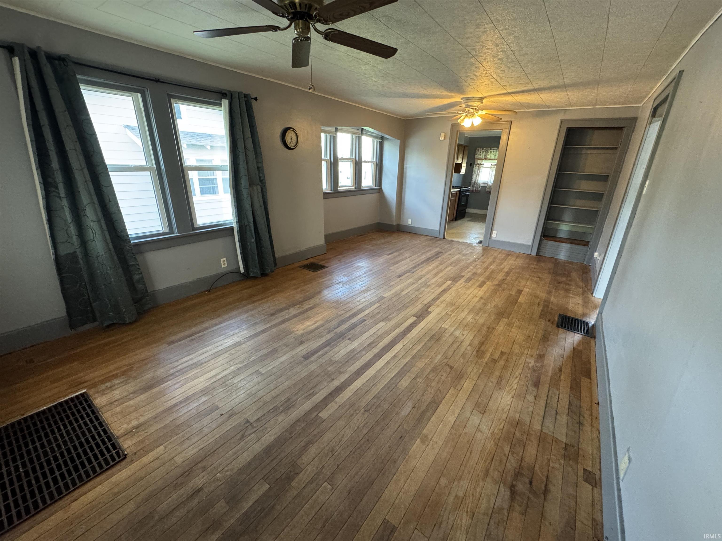 Spacious room featuring wood-finish flooring, multiple windows providing natural light, a ceiling fan, and built-in shelving