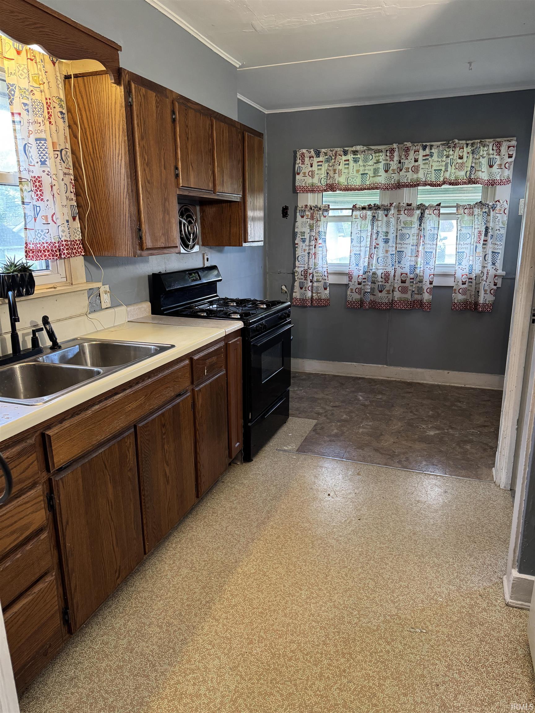 Kitchen featuring wood-finish cabinetry, a double basin stainless steel sink, and a black gas range