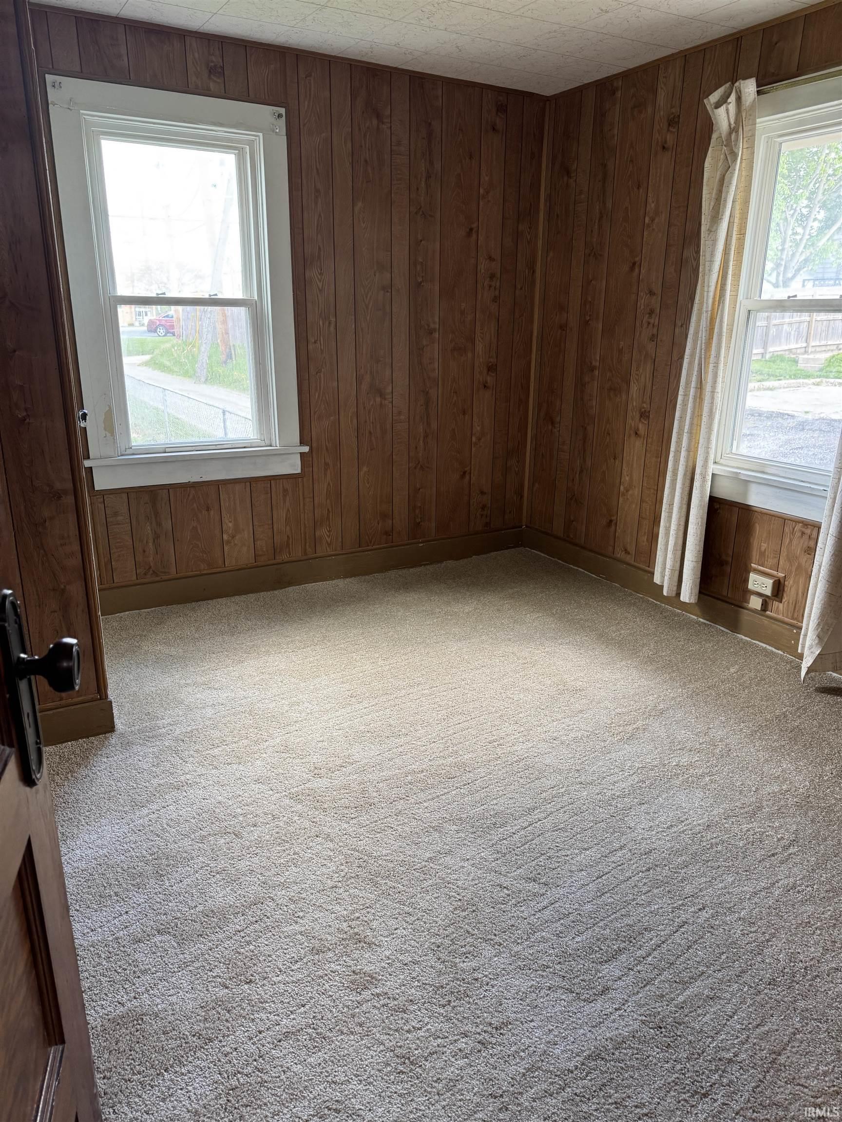 Carpeted room featuring wood-paneled walls and multiple windows with white trim