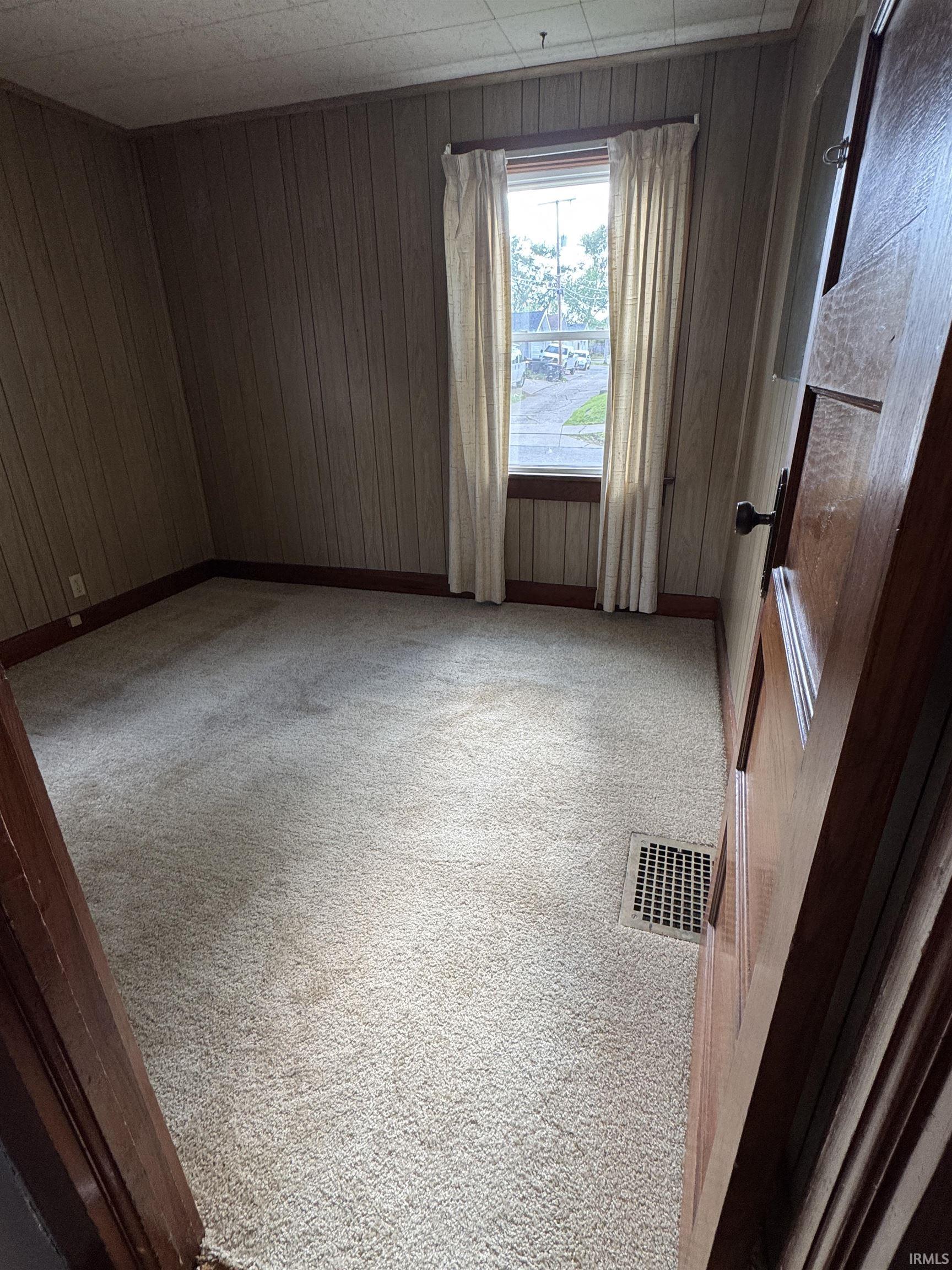 Carpeted interior room featuring vertical paneled wall treatments and a single window with curtain rods