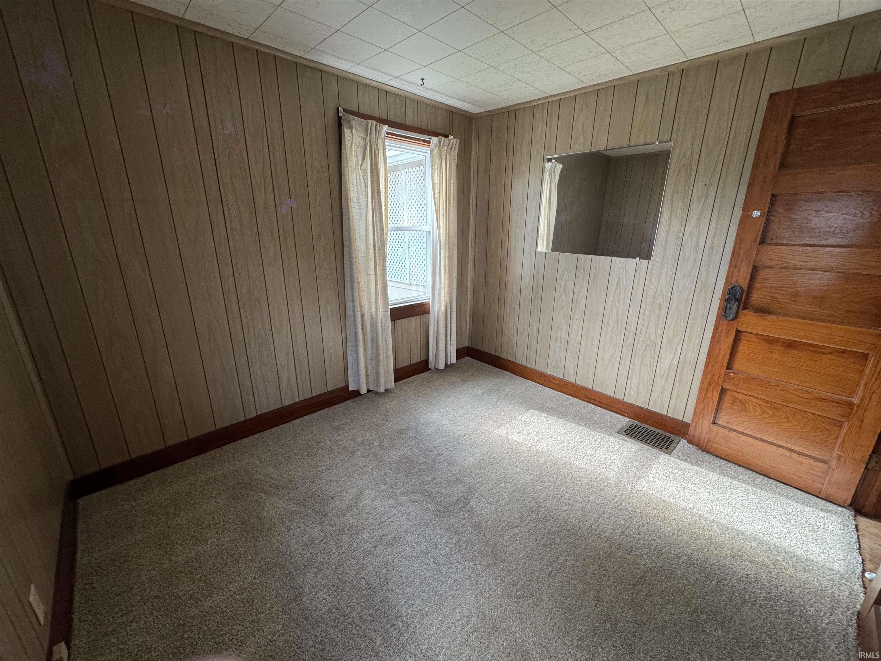 Carpeted room featuring wood-panel walls, a single window, and a paneled wood door