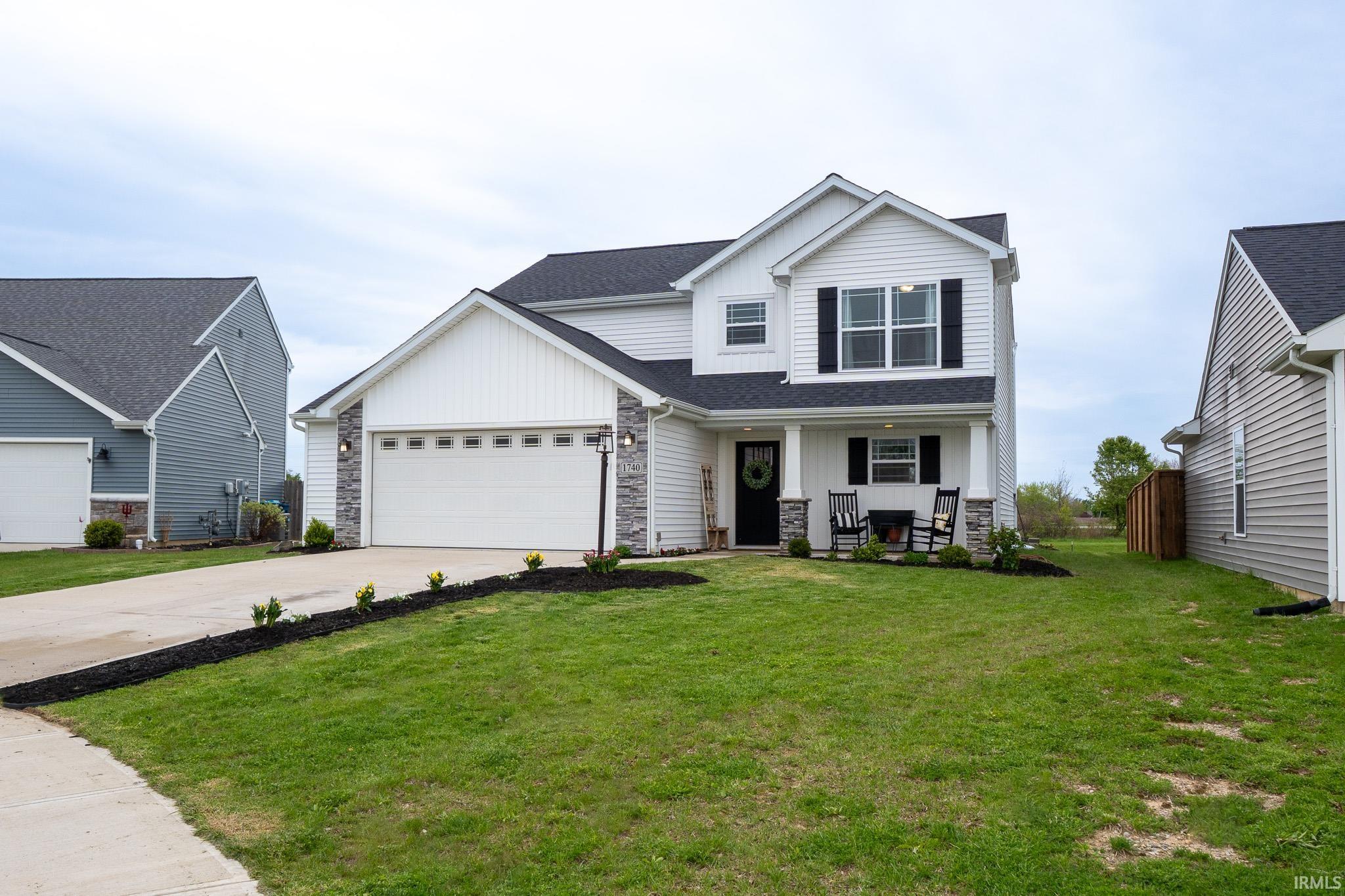 Two-story white residence featuring a dark roof, attached garage, and a covered porch