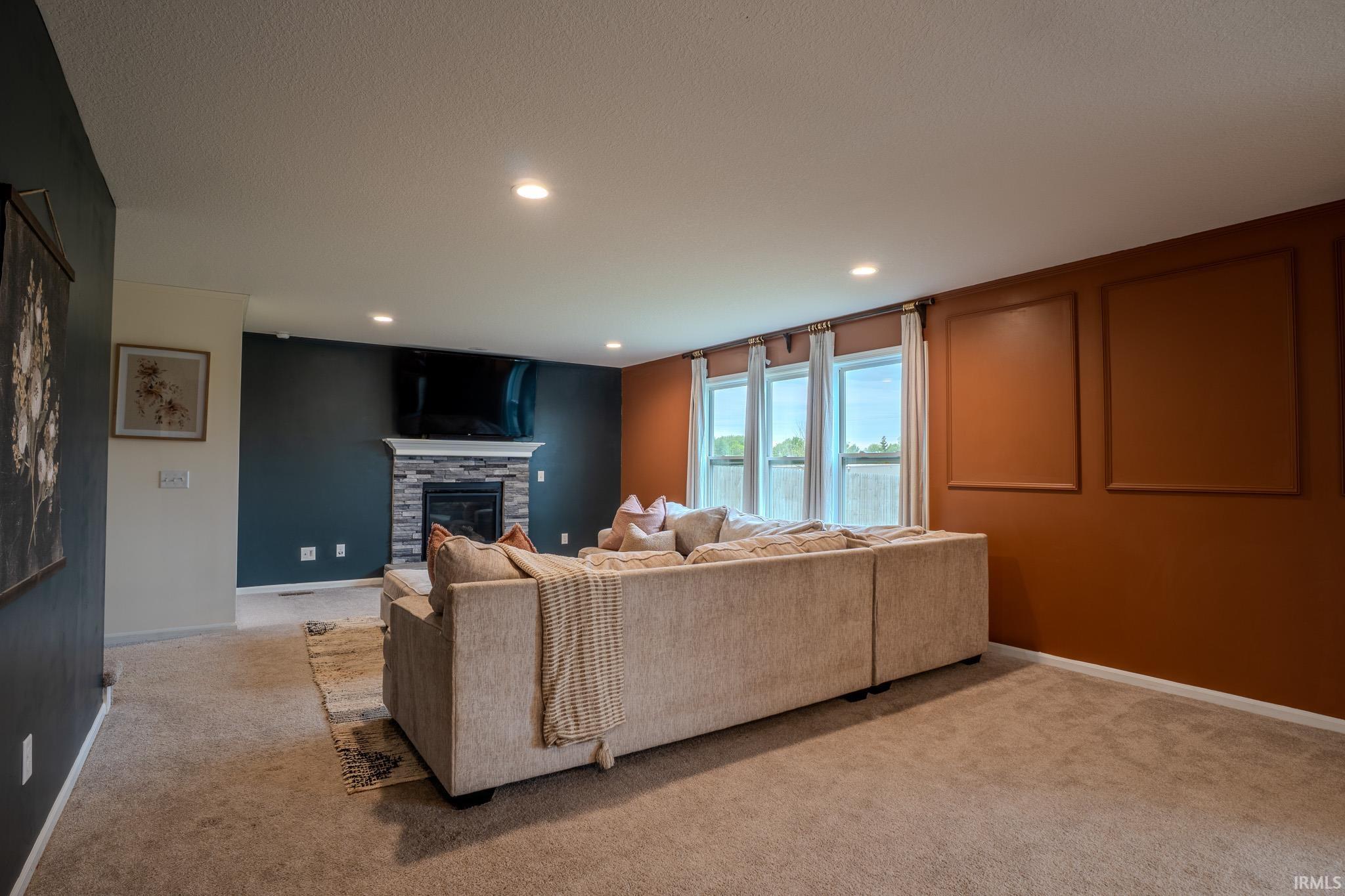 Living area featuring plush carpeting, a stone-clad fireplace with a white mantel, and recessed lighting
