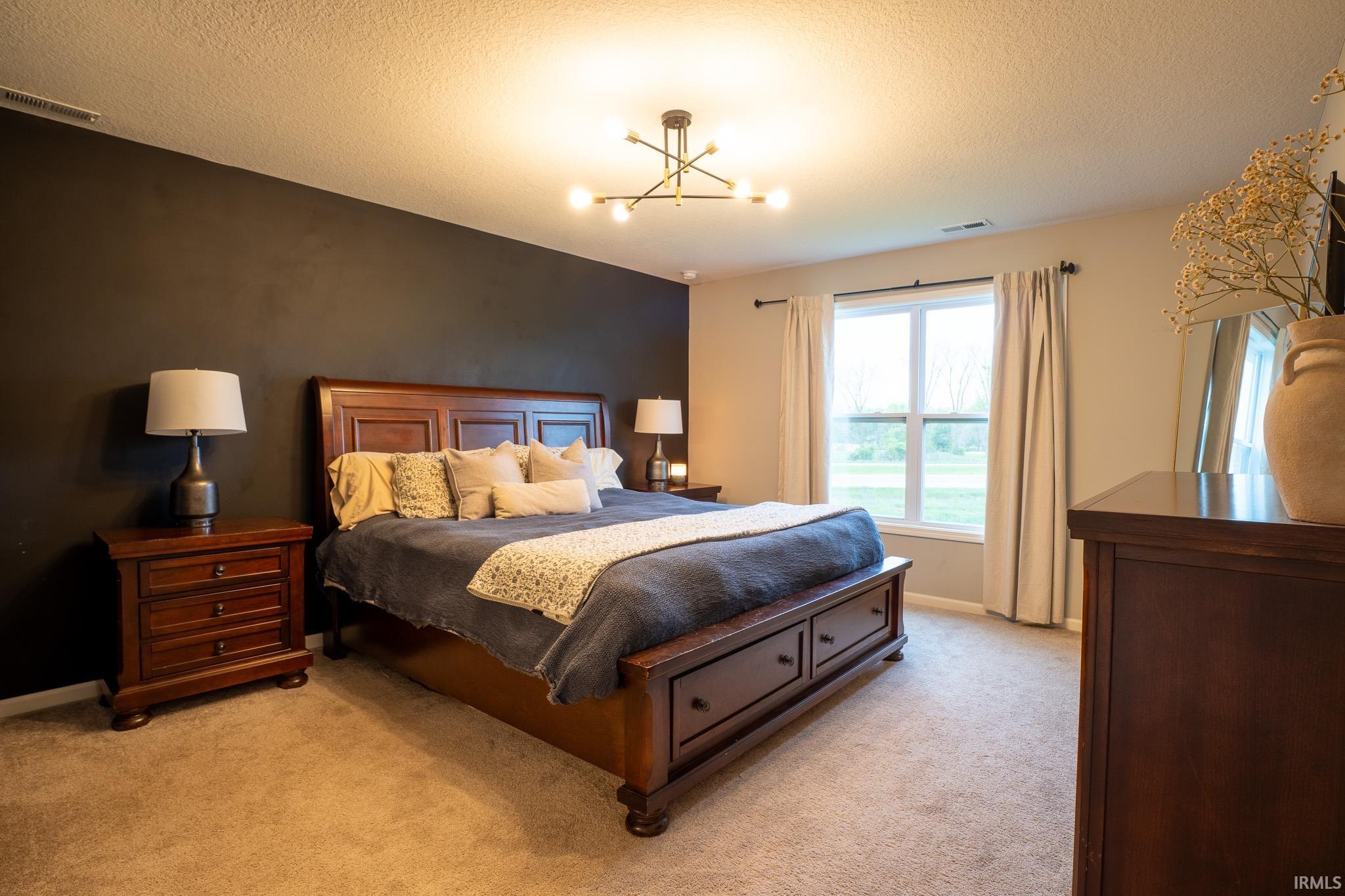 Spacious bedroom with dark accent wall, plush carpeting, large window with ample natural light, and a contemporary ceiling light fixture