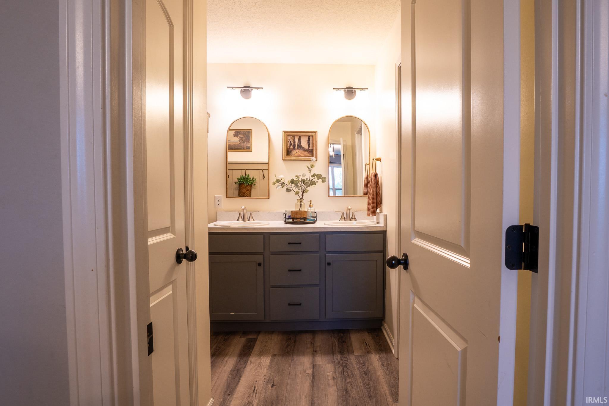 Bathroom featuring a double vanity with gray cabinetry, white countertops, dual sinks with chrome fixtures, and wood-finish flooring