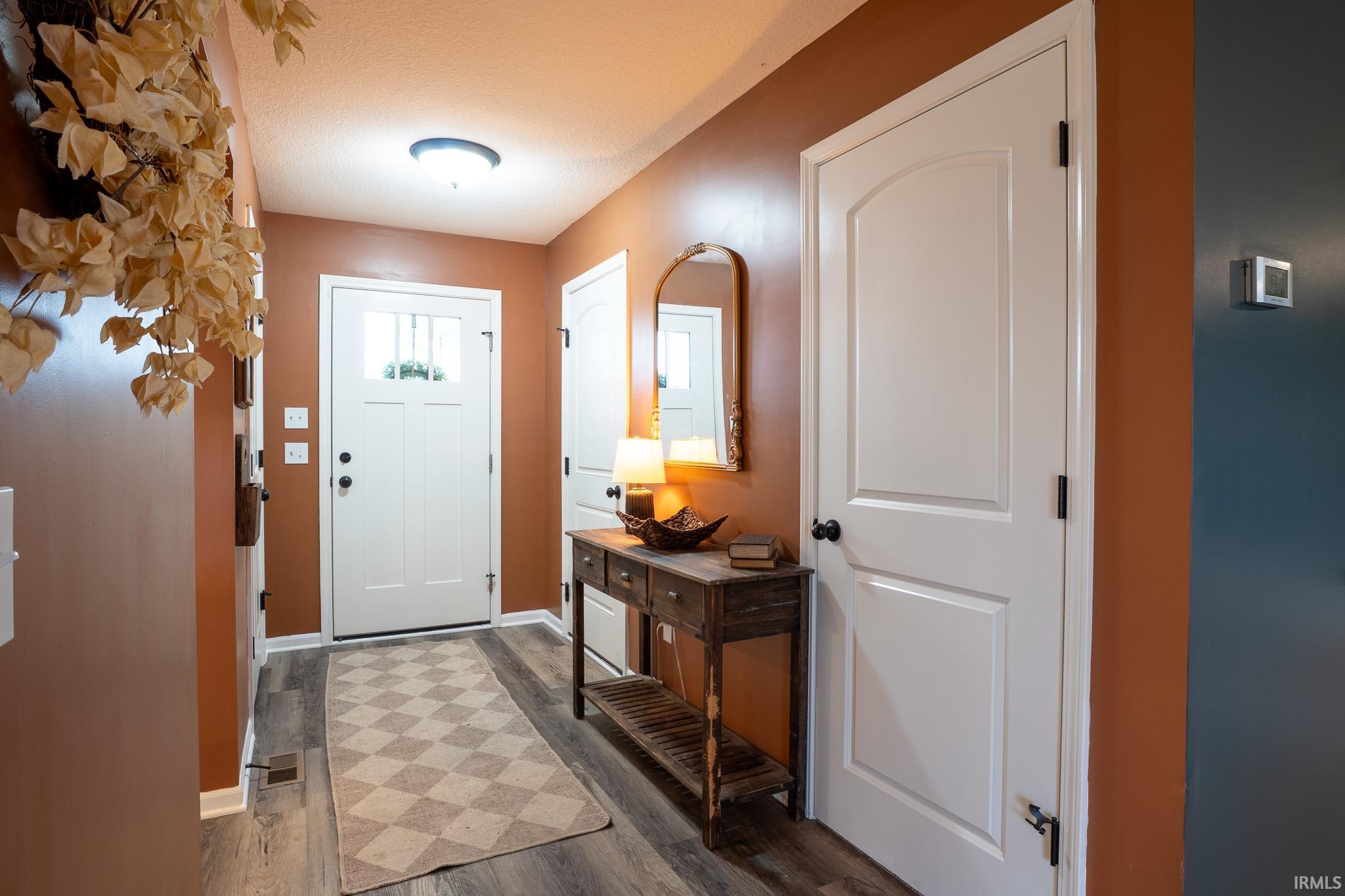 Inviting entryway featuring a white paneled door with glass inserts, wood-finish flooring, a built-in overhead light fixture, and a white interior door with an arched panel detail