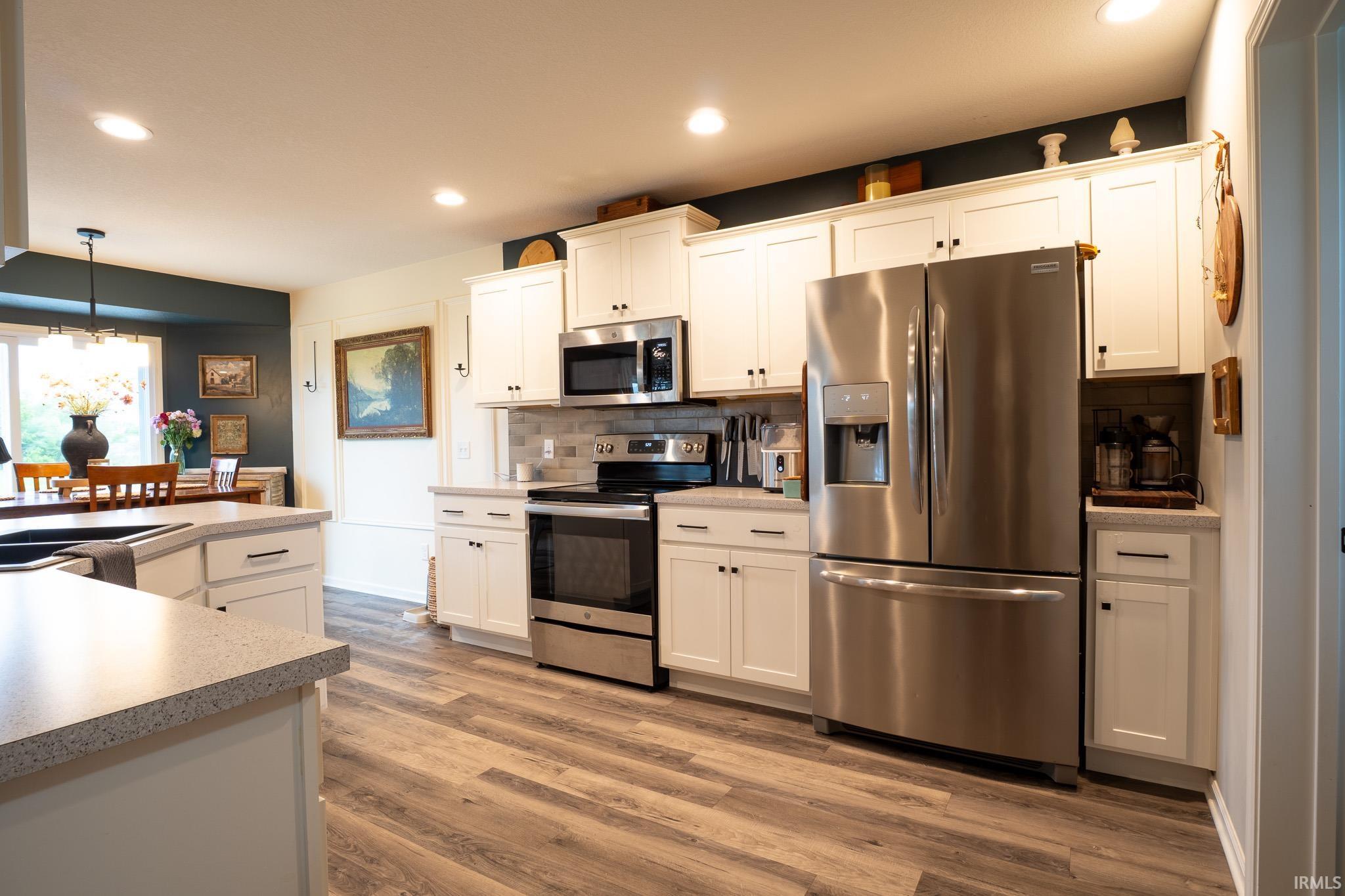 Bright kitchen featuring white cabinetry, wood-finish flooring, a stainless steel appliance suite, light-toned countertops, and recessed lighting