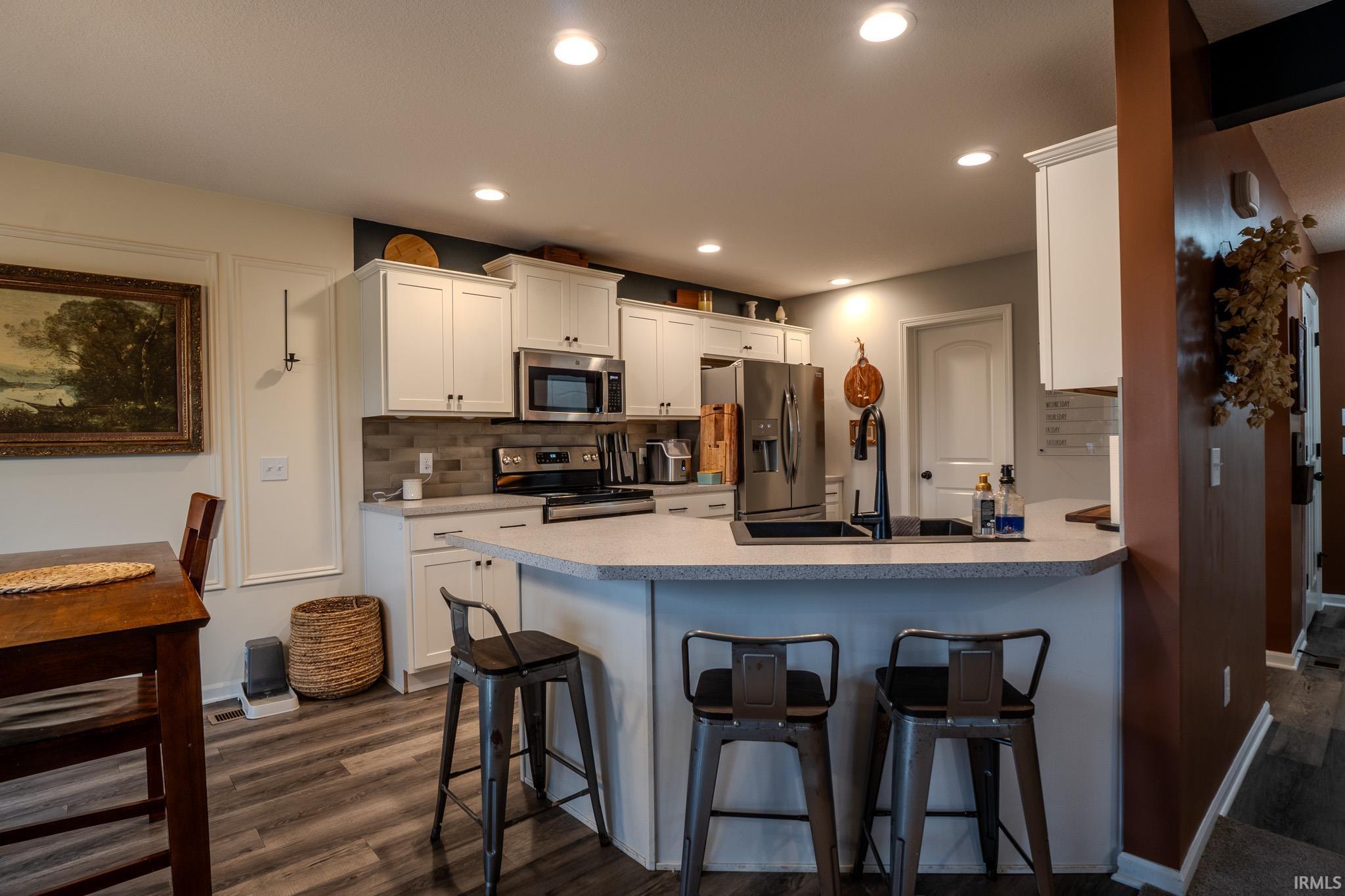 Well-appointed kitchen featuring white cabinetry, stainless steel appliances, a tiled backsplash, and light-toned countertops with a breakfast bar