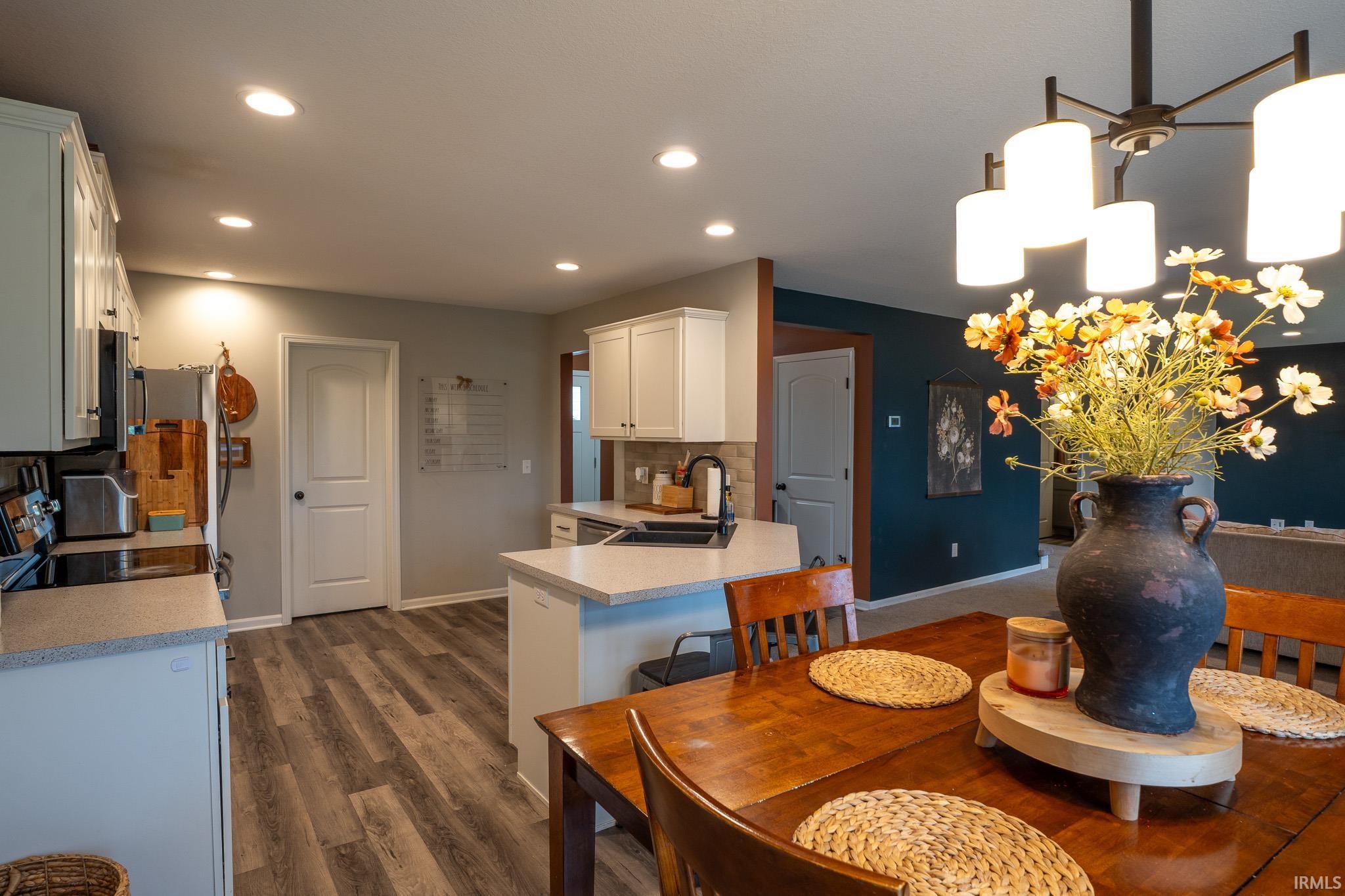 Open-concept kitchen and dining area featuring recessed lighting, light-toned cabinetry, wood-finish flooring, a kitchen island with stone-look countertop, and a contemporary dining chandelier