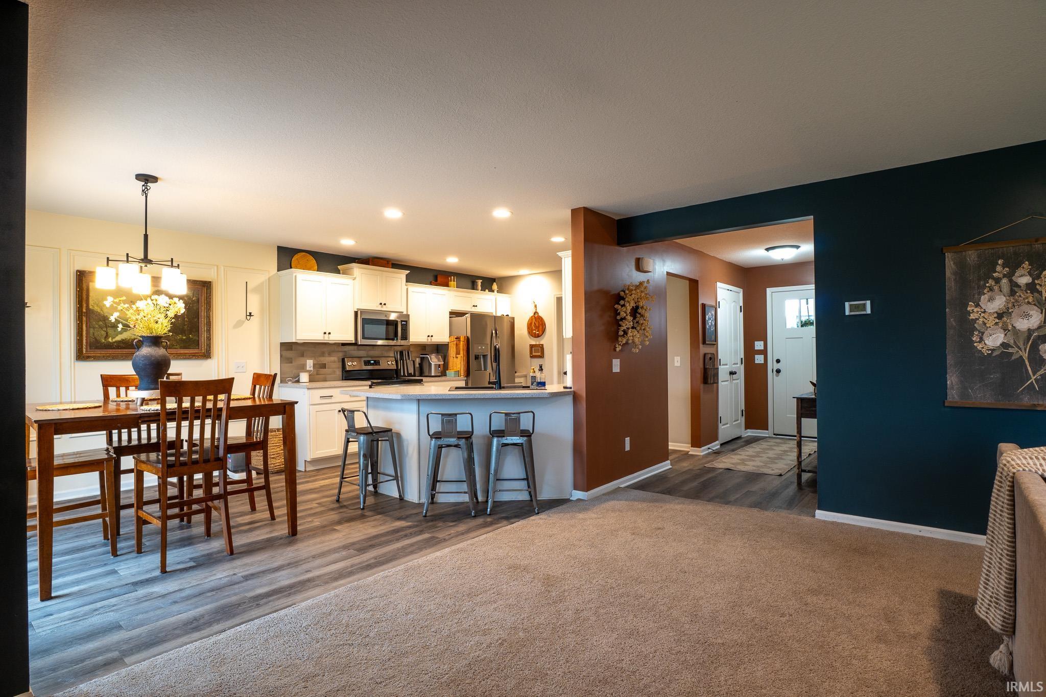 Open-concept living space featuring a kitchen with white cabinetry and stainless steel appliances, a dining area with a linear chandelier, and wood-finish flooring