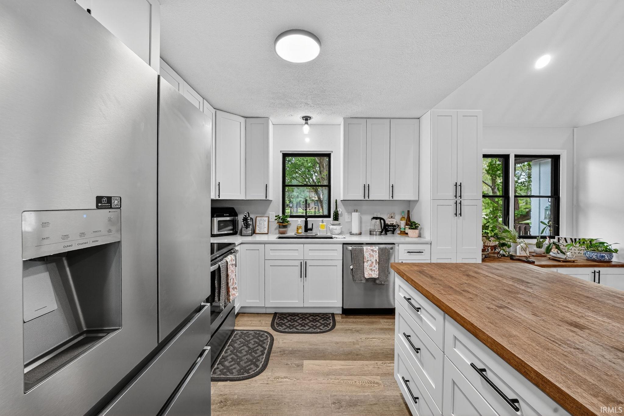 Modern kitchen featuring white shaker cabinetry, stainless steel appliances, and wood-finish flooring