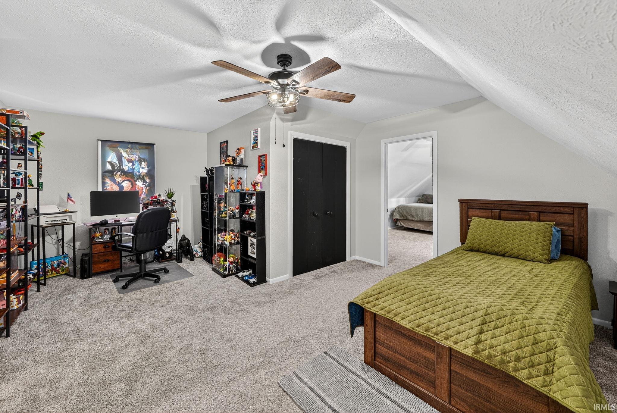 Carpeted room with a ceiling fan, sloped attic walls, and a wood bed frame