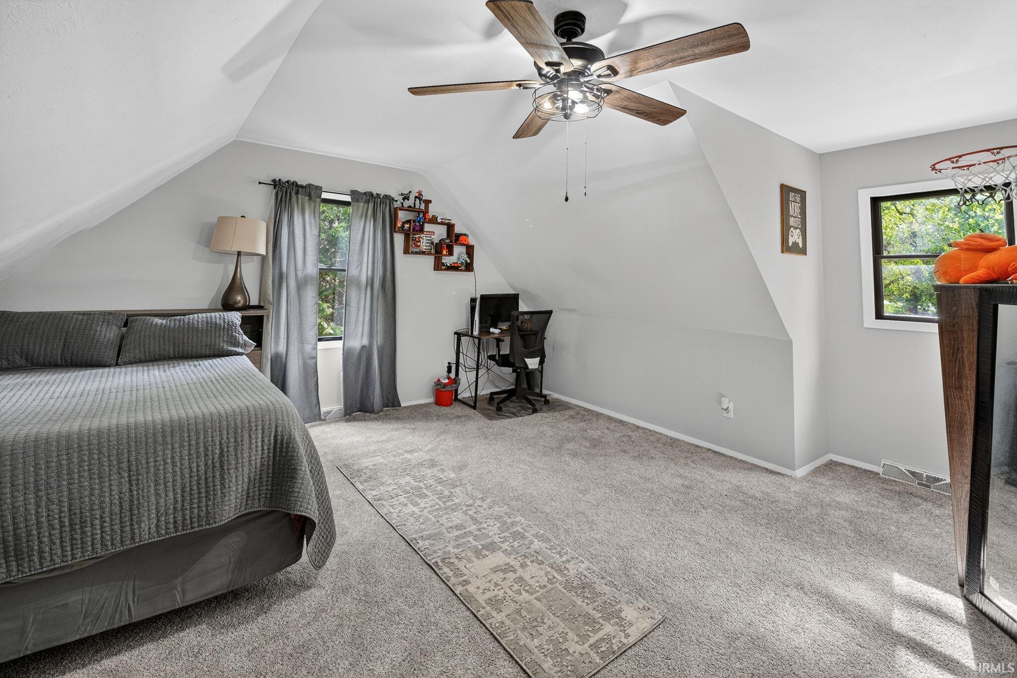 Vaulted ceiling bedroom featuring carpeting, a ceiling fan, and multiple windows