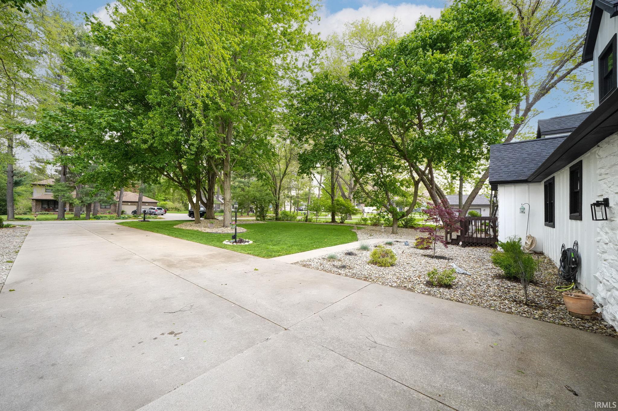 Expansive concrete driveway with a manicured lawn area and mature trees