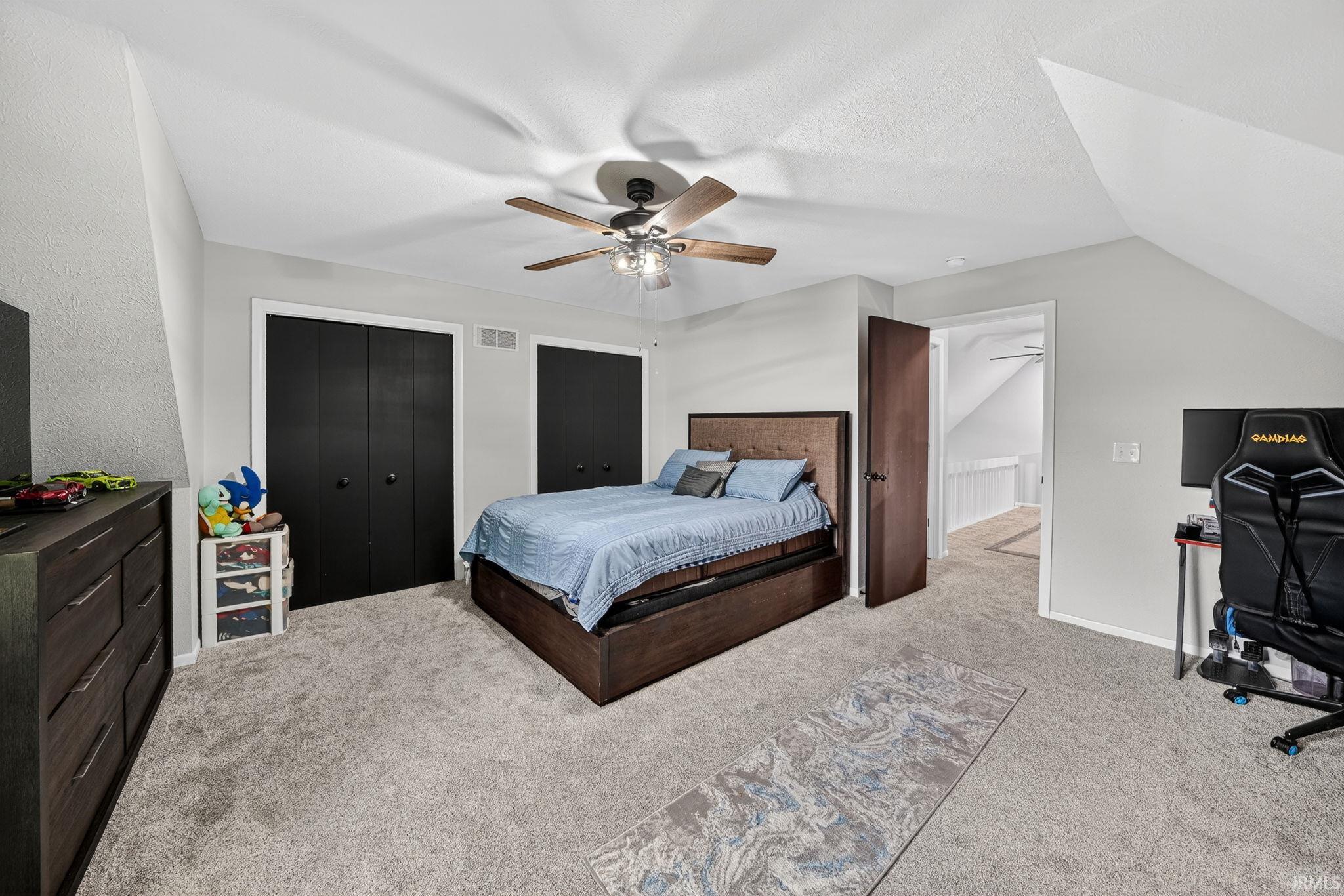 Spacious room featuring sloped ceilings, two sets of bi-fold closet doors, a ceiling fan with integrated lighting, and light gray wall paint