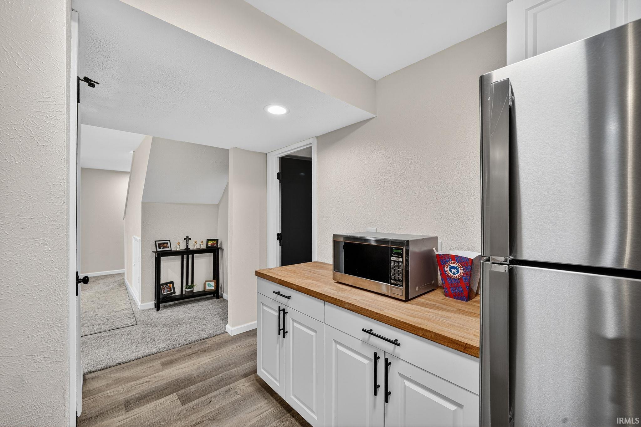 Compact kitchen area featuring white shaker-style cabinetry, wood-finish countertops, and a stainless steel refrigerator