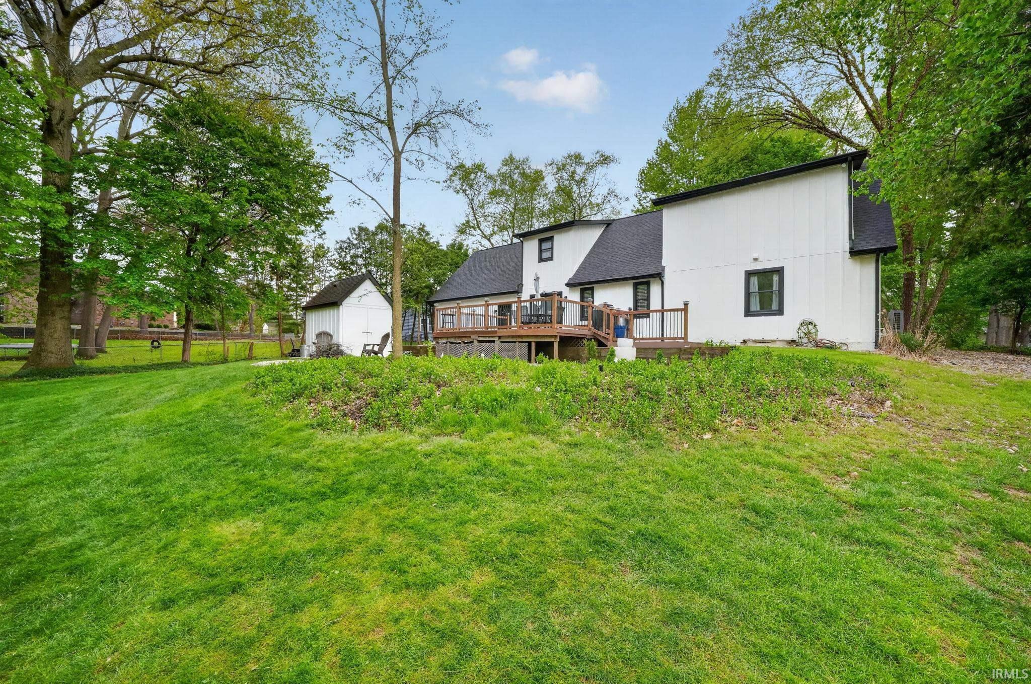 Expansive backyard with a manicured lawn, mature trees, and a multi-level wood deck