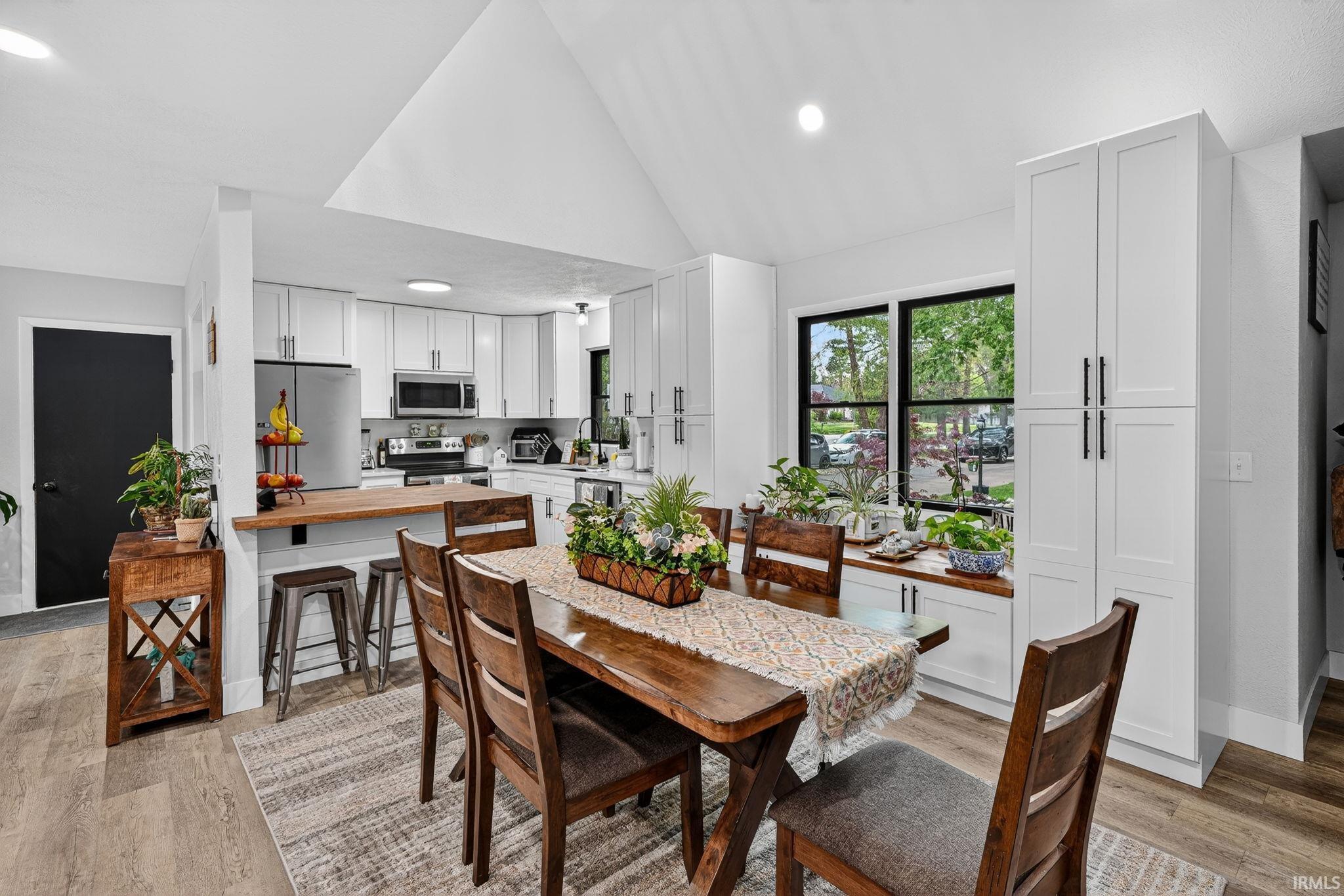 Open-concept kitchen and dining area featuring a vaulted ceiling and wood-finish flooring