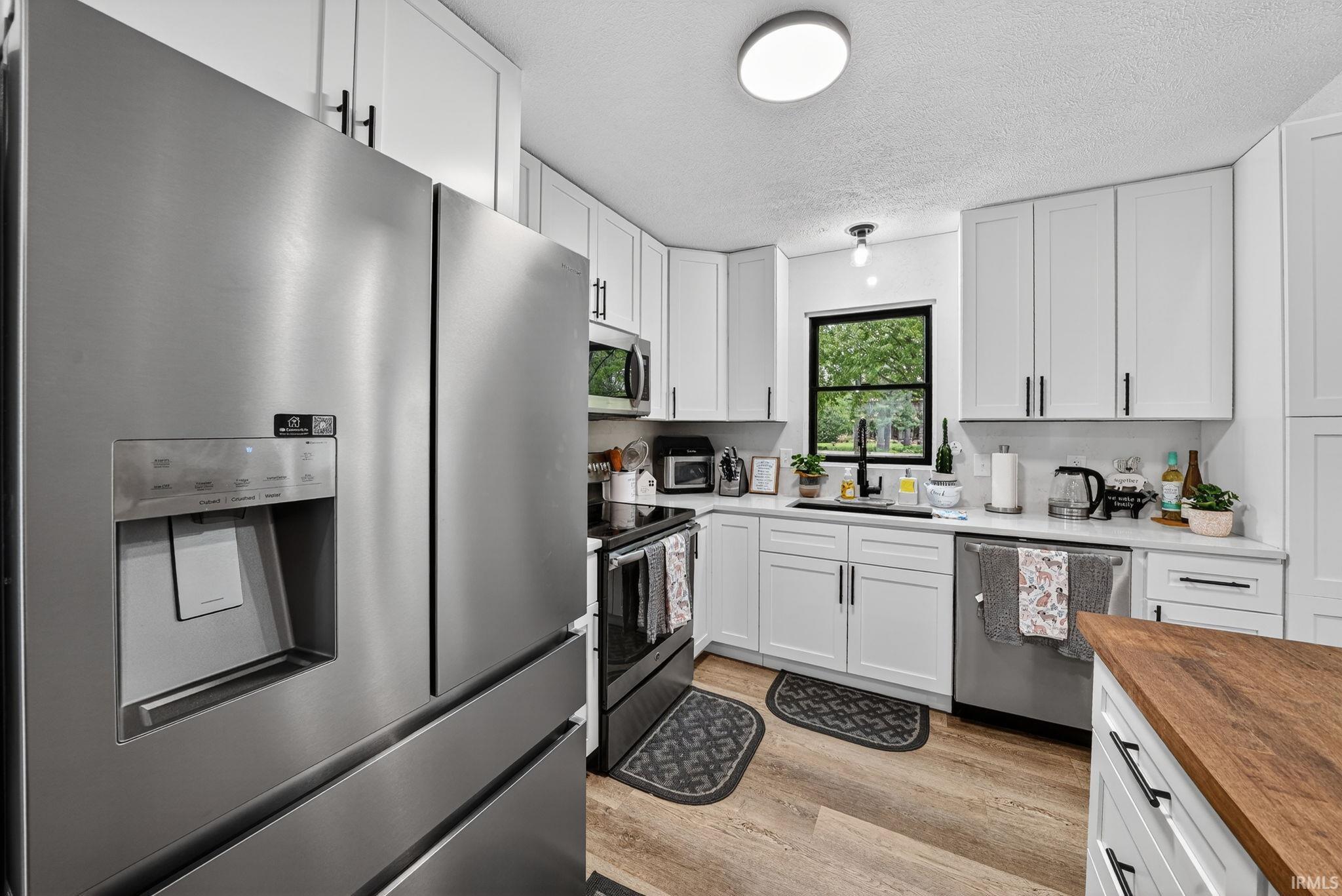 Modern kitchen featuring white shaker cabinetry with matte black hardware, stainless steel appliances, wood-finish flooring, and light-toned countertops