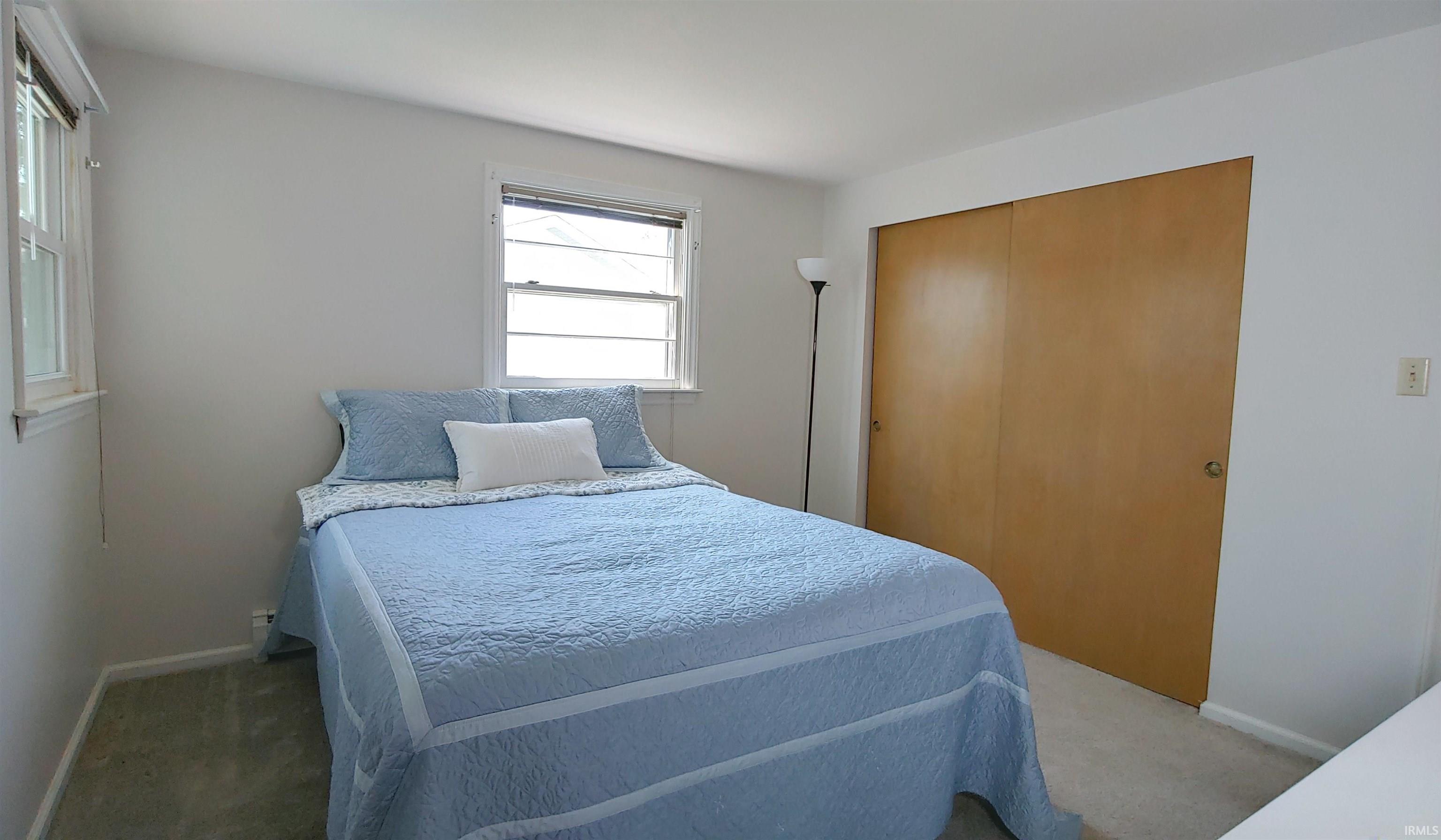 Room featuring light-colored walls, two double-hung windows with sills, wall-to-wall carpeting, and a full-height closet with bi-fold wood-panel doors