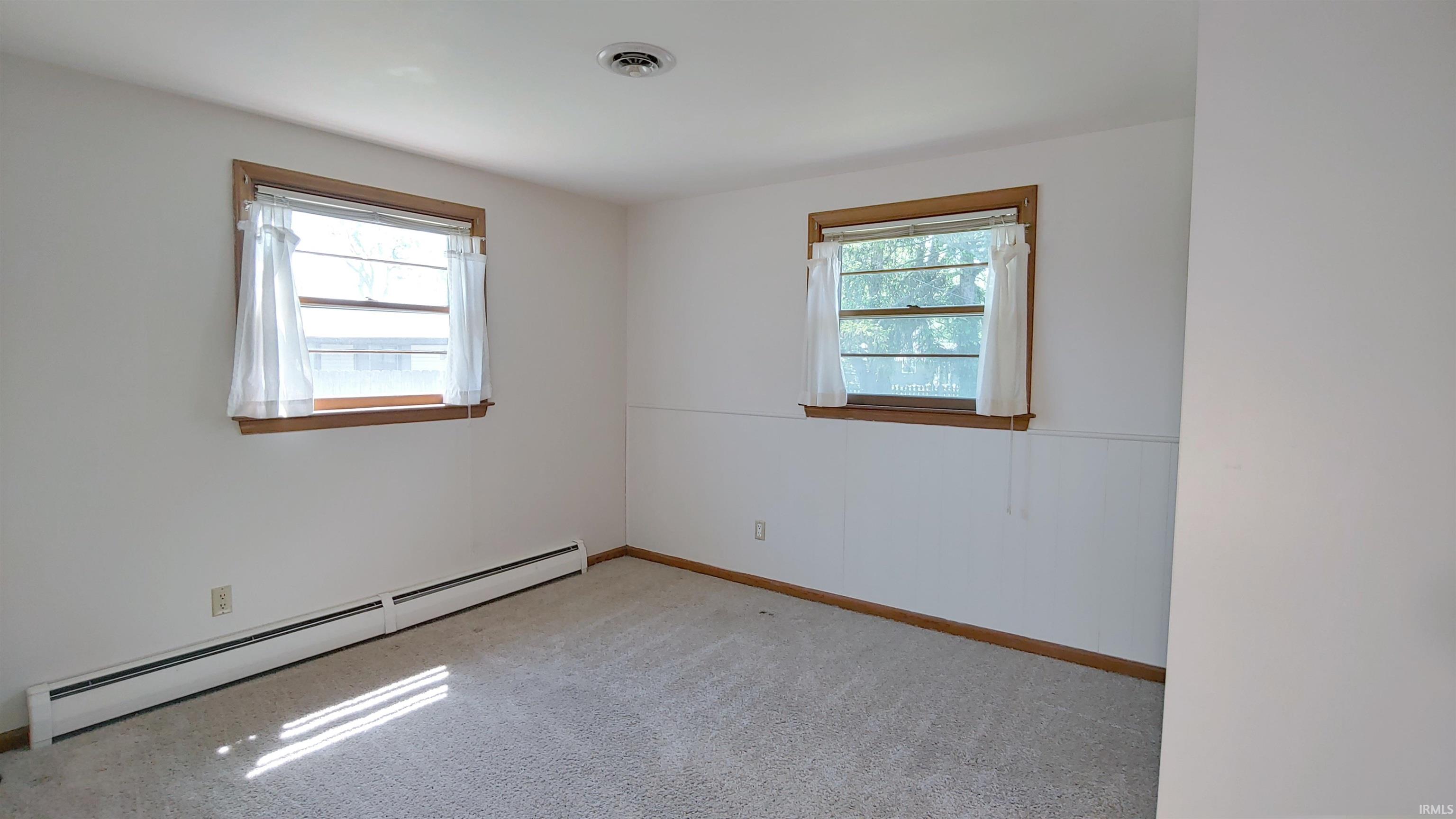 Carpeted room with two windows featuring wood trim