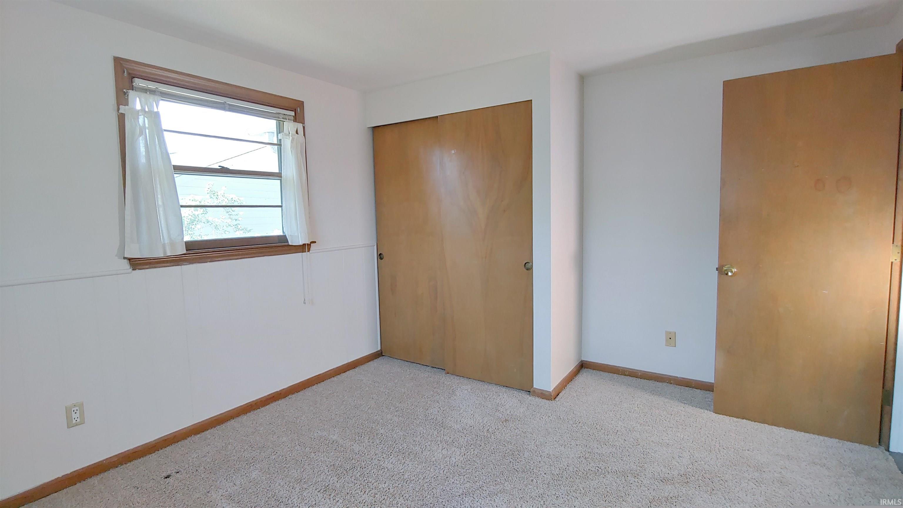 Carpeted room featuring a window with wood trim, wood baseboards, and a bi-fold closet door.
