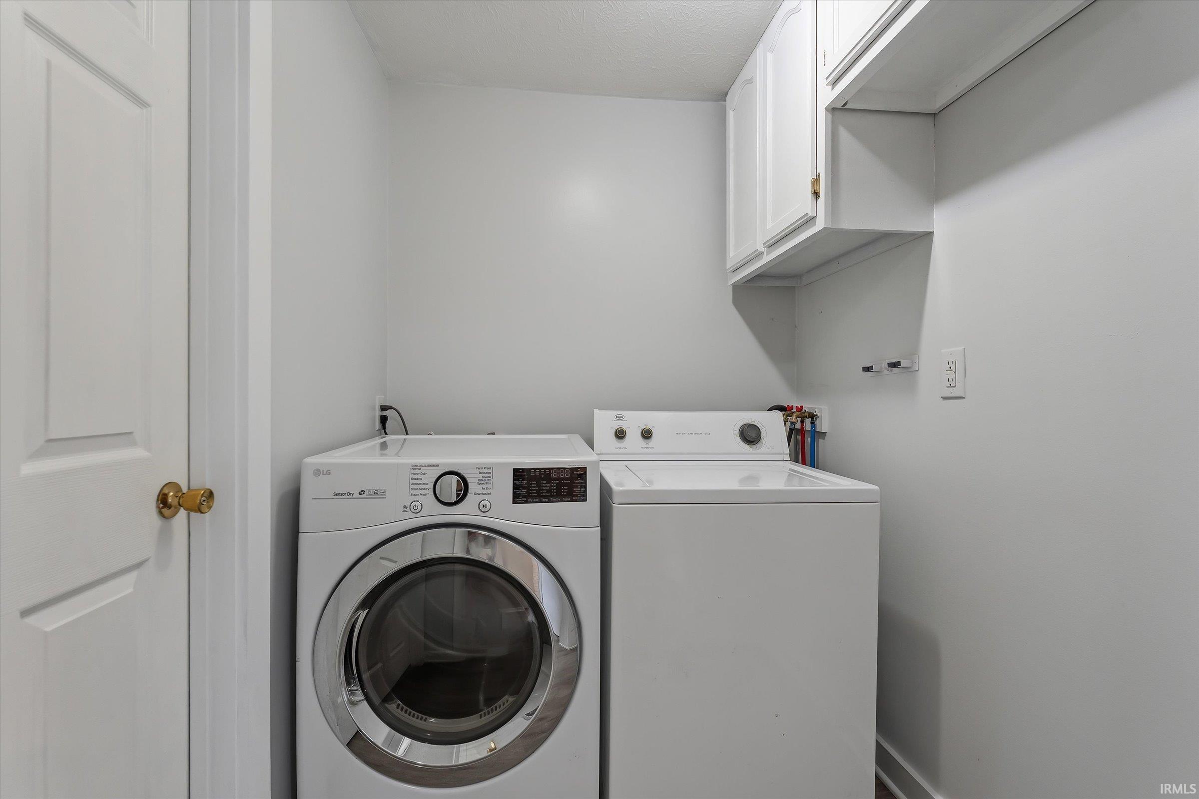 Dedicated laundry area featuring white cabinetry, an open storage shelf, and a painted paneled door with brass hardware