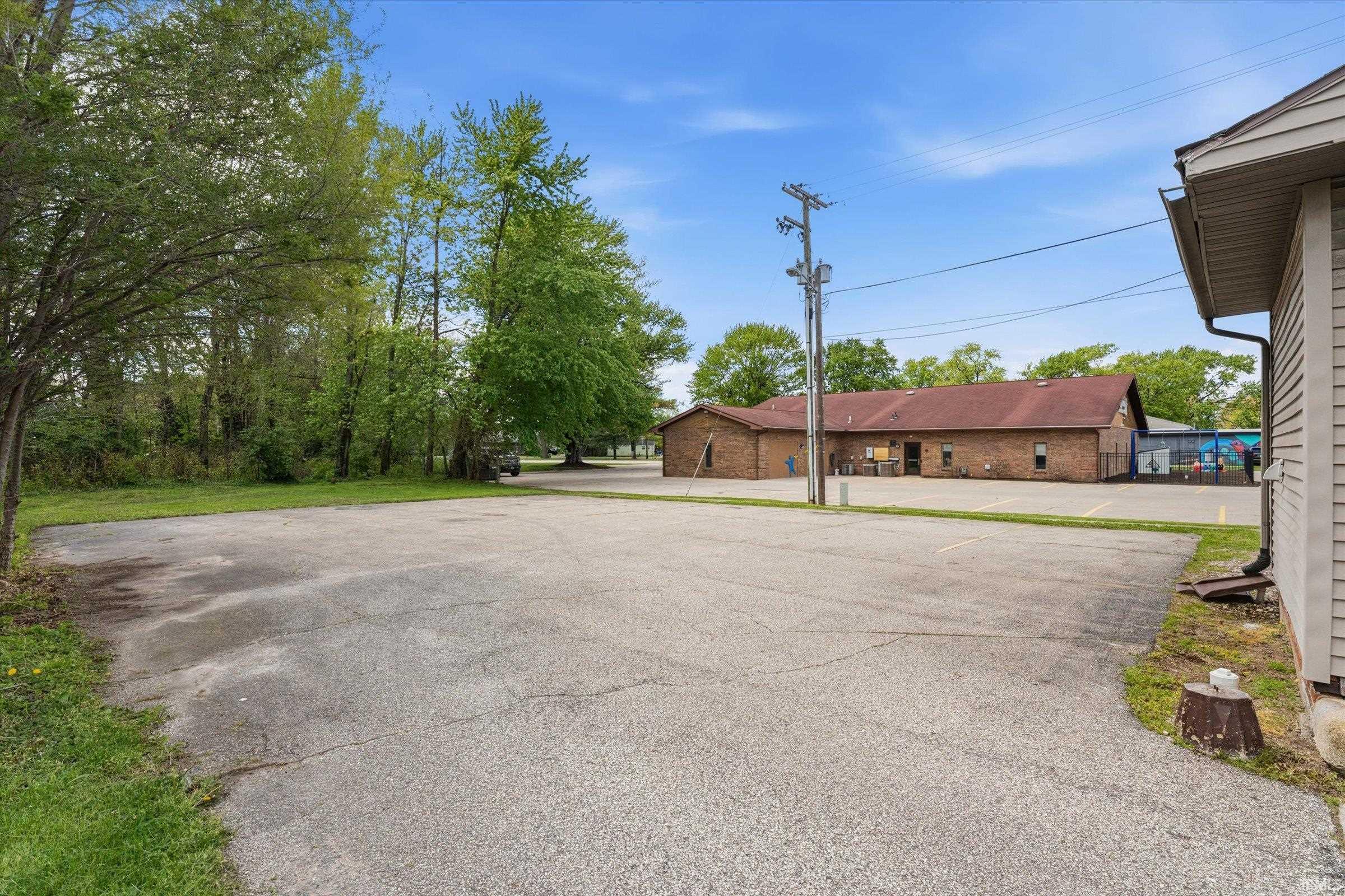 Expansive asphalt parking area with ample space, bordered by mature trees and green landscaping